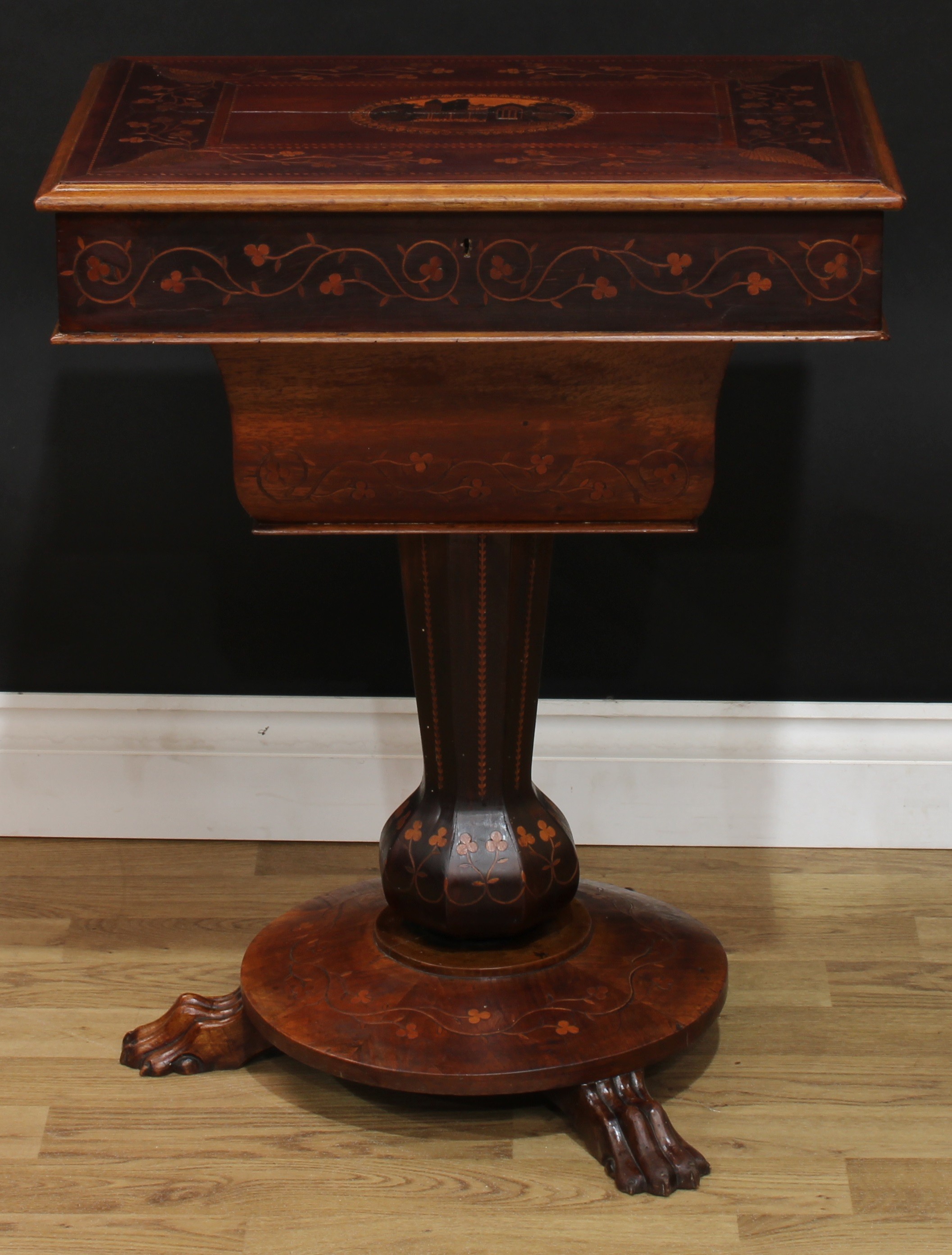 A 19th century Irish Killarney marquetry and arbutus work table, hinged cover, adjustable on a ratchet, inlaid with an oval reserve of Muckross Abbey, County Kerry, Ireland, bordered by trailing sprays of seamróg shamrocks, outlined throughout with barber-pole stringing, the verso inlaid with a cláirseach or Celtic harp, serpentine cushion-moulded well, panelled 'garlic-mouth' column, circular base, inlaid throughout with clover, claw feet, 71cm high, 56.5cm wide, 41cm deep, c.1850