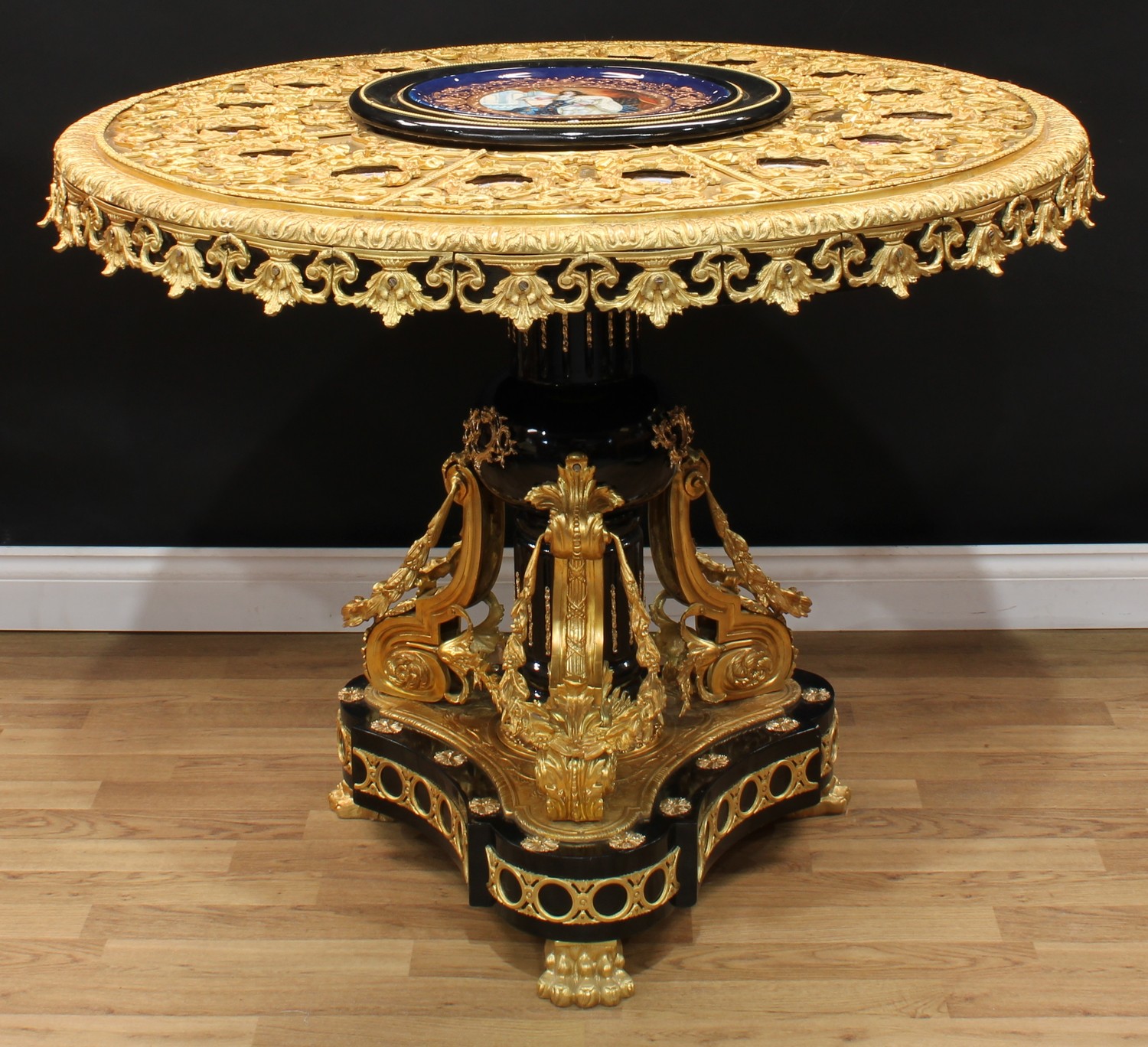 A Louis XVI design gilt metal and porcelain mounted guéridon or centre table, circular top with inset porcelain plaques, decorated in the manner of Sèvres, each portrait oval framed with a ribbon-tied swag of fruiting leaves, stiff acanthus border, fluted column, incurve rounded triform base, lion paw feet, 88cm high, 111cm diameter, third-quarter 20th century