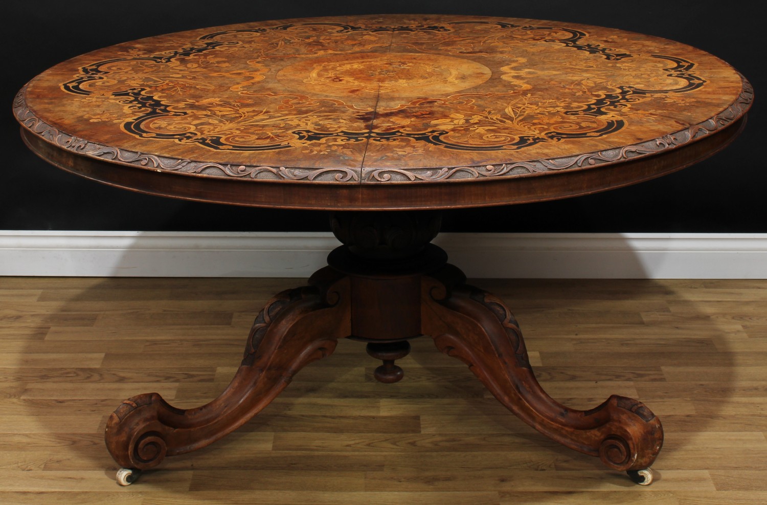 A Victorian walnut and marquetry centre table, circular top with foliate carved edge, profusely inlaid in specimen timbers with flowers and foliage, baluster column, cabriole legs, turned underfinial, scroll feet, ceramic casters, 74cm high, 142cm diameter, c.1860