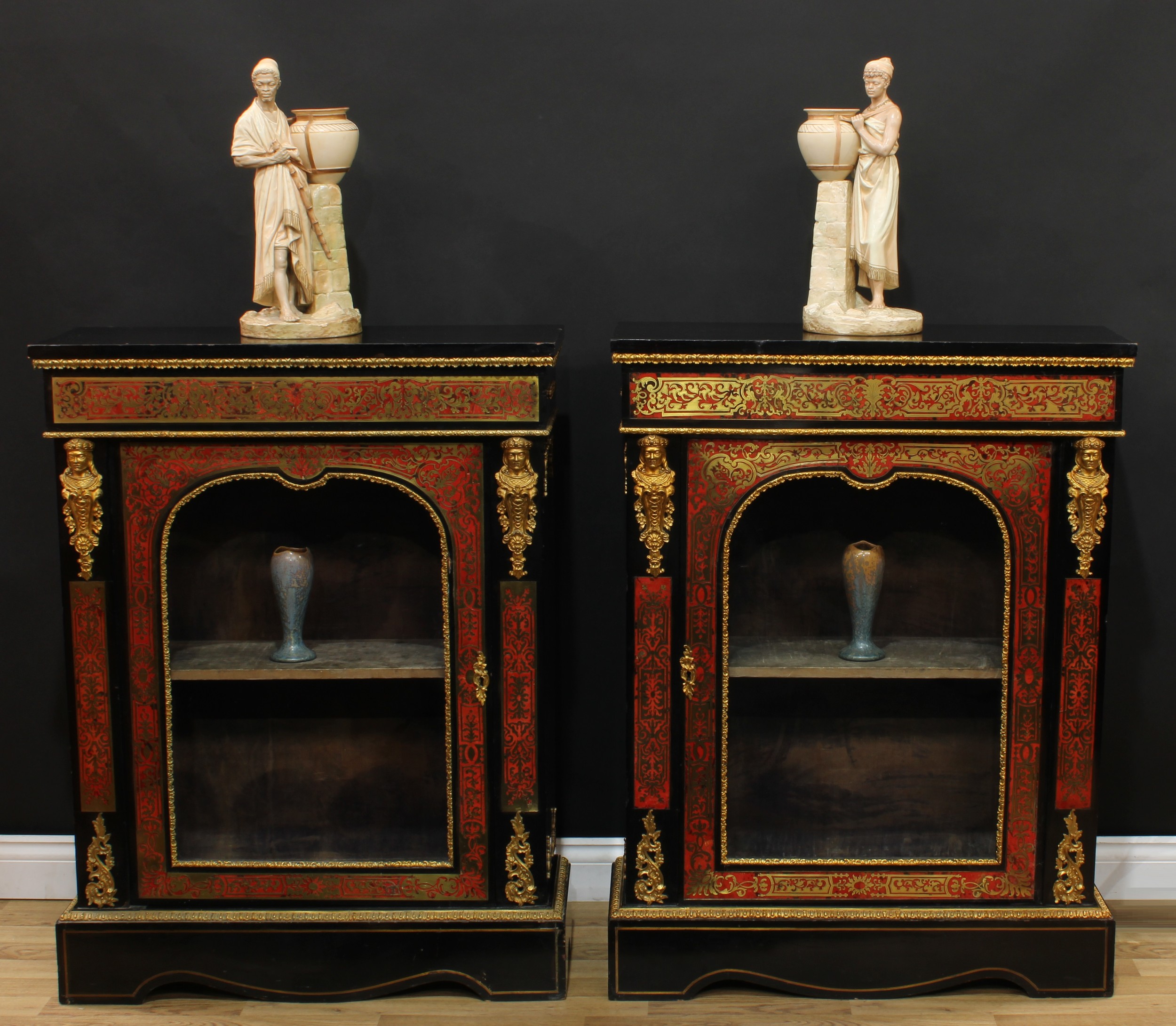 A pair of 19th century gilt metal mounted Boulle and ebonised pier cabinets, each rectangular top above a deep frieze and an arched glazed door flanked by masks, shaped plinth bases, 109cm high, 83cm wide, 30.5cm deep, c.1880