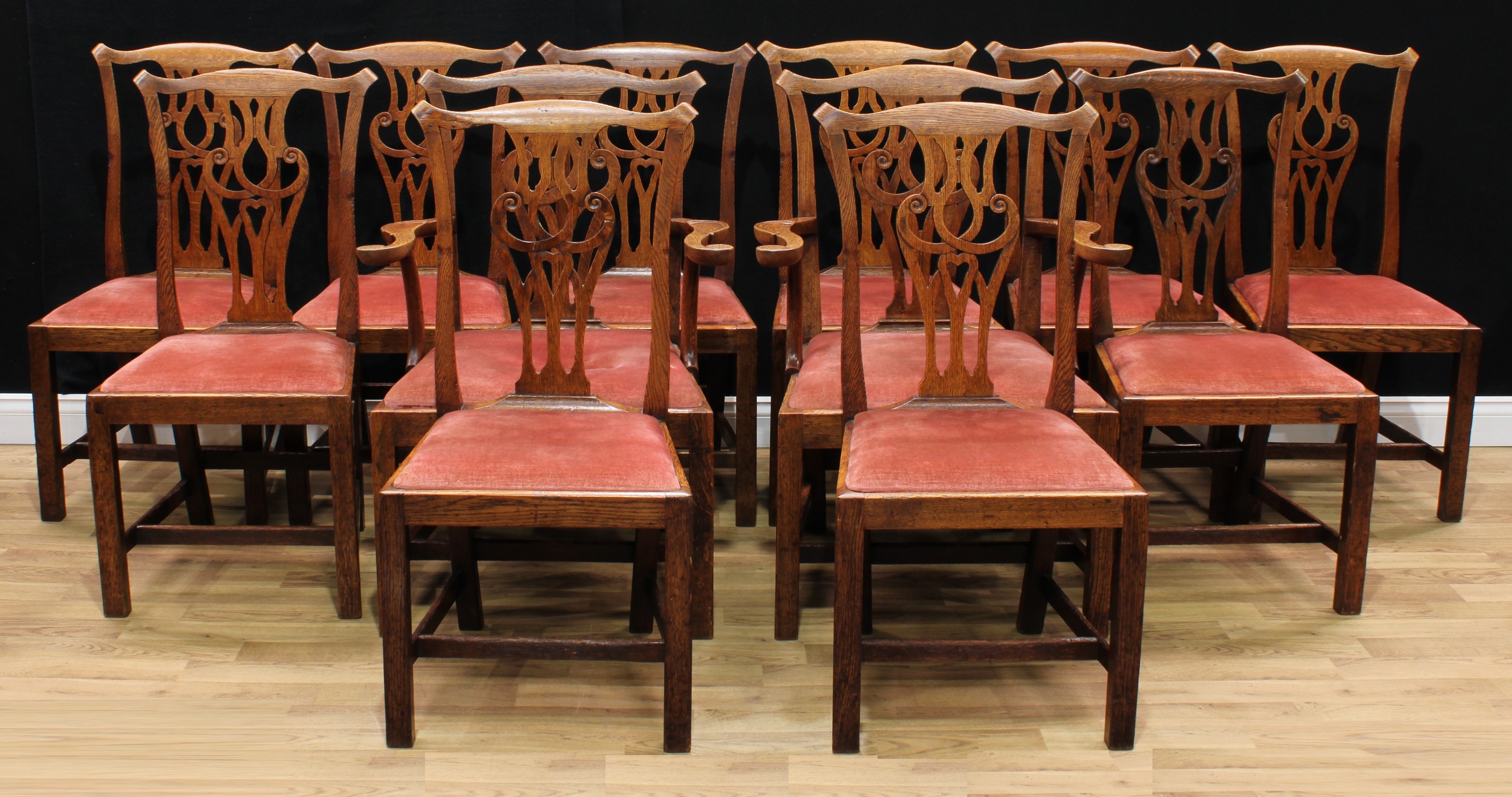 A set of twelve Provincial Chippendale Revival oak dining chairs, comprising a pair of carvers and ten side chairs, Cupid's bow cresting rails, shaped and pierced splats centred by heart motifs, drop-in seats, square legs, H-stretchers, the carver 96cm high, 66.5cm wide, the seat 46cm wide and 44cm deep, the side chair 95.5cm high, 49cm wide, the seat 40cm wide and 36cm deep, 19th century