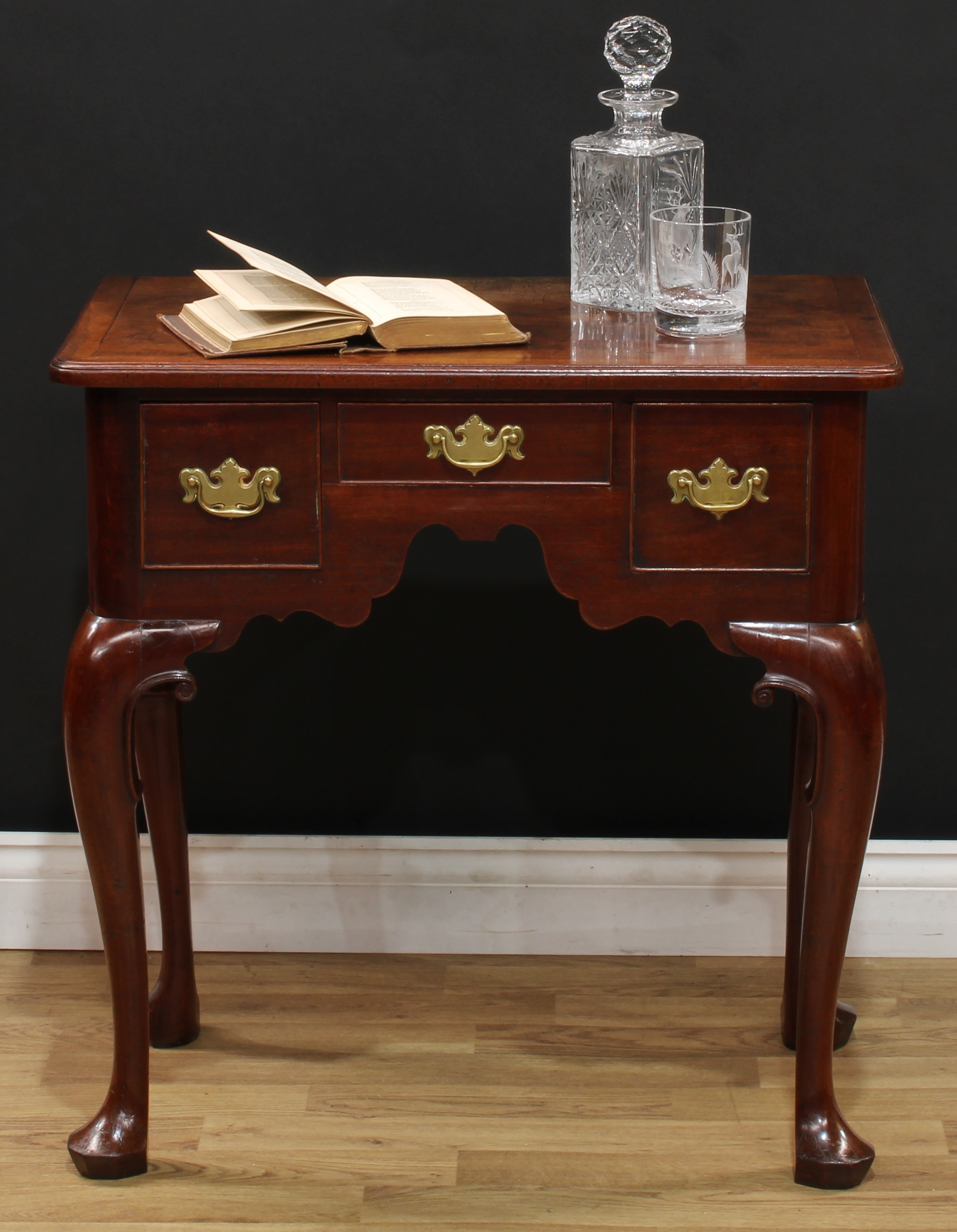 A George II mahogany lowboy, possibly Irish, oversailing rectangular top with moulded edge above three cockbeaded frieze drawers, brass swing handles, brass bat wing escutcheons, shaped apron, cabriole legs carved to the knees with scrolls, faceted pad feet, 72.5cm high, 72cm wide, 43cm deep, c.1745