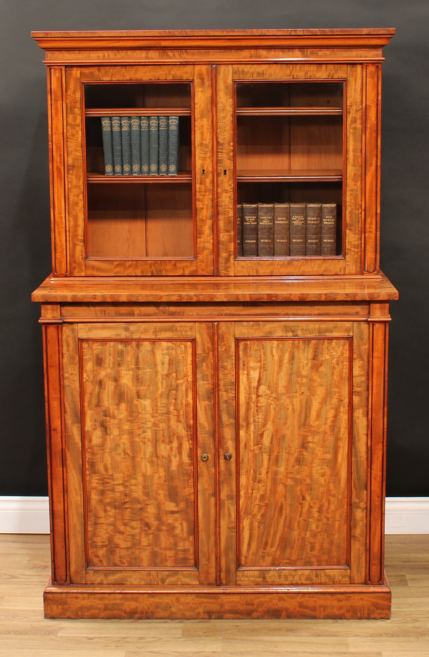 A Post-Regency gonçalo alves library cabinet, by Gillow of Lancaster, stamped, of small and neat proportions, the bookcase upper stage with moulded cornice above a pair of glazed doors enclosing adjustable shelves, the projecting base with a pair of panel doors enclosing five drawers and further adjustable shelves, plinth base, 160cm high, 96cm wide, 47.5cm deep, Bramah locks, c.1830