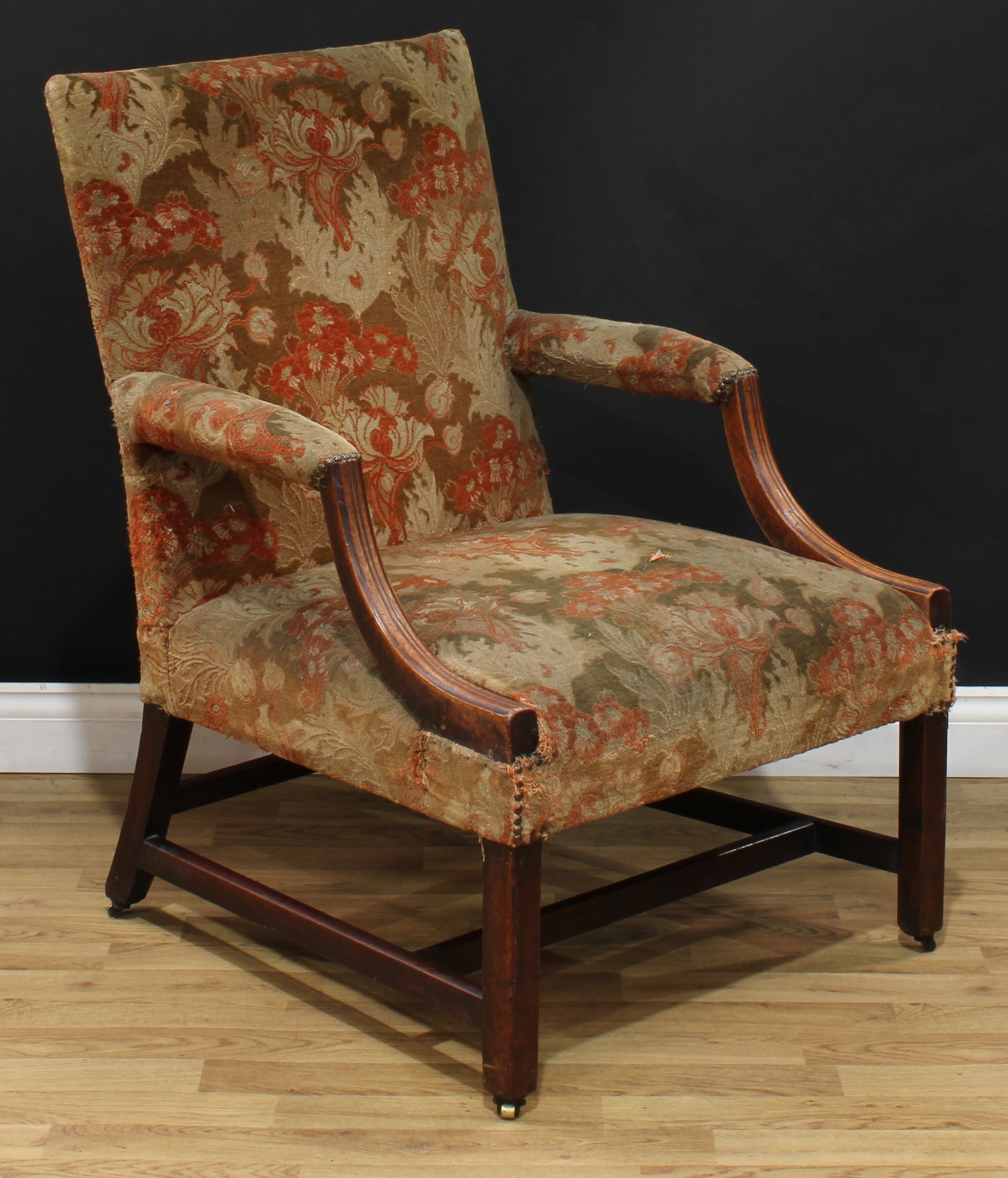 A George III mahogany Gainsborough armchair, stuffed-over upholstery, moulded downswept arms, chamfered legs, H-stretcher, brass casters, 99cm high, 69cm wide, the seat 57cm wide and 55cm deep, c.1800