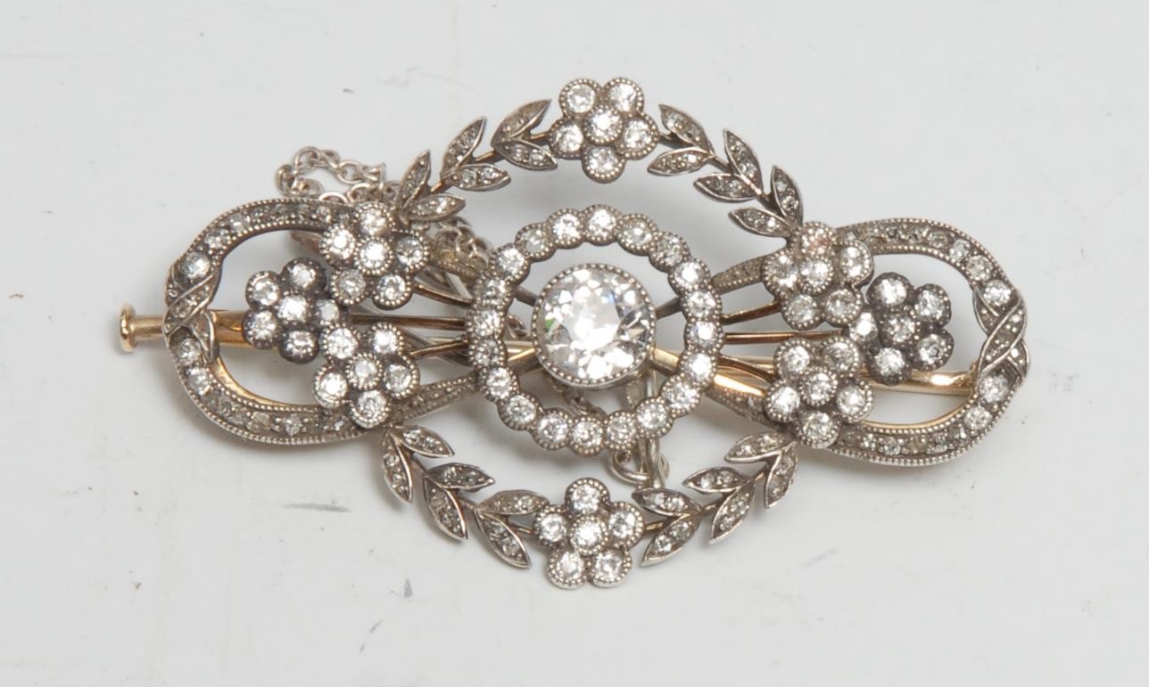 A gold and platinum diamond brooch, the central stone approx 0.50ct surrounded by a garland of diamond accented five petal flowers, unmarked yellow and white metal mount with safety chain, 44mm wide, 7.19g gross, boxed