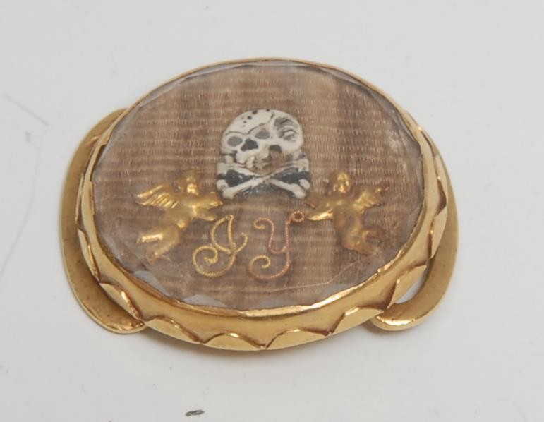A late 17th/early 18th century gold coloured metal, rock crystal and plaited hair oval momento mori mourning slide, decorated with skull-and-crossbones and initials GY, 2cm wide, c.1700, 6g gross