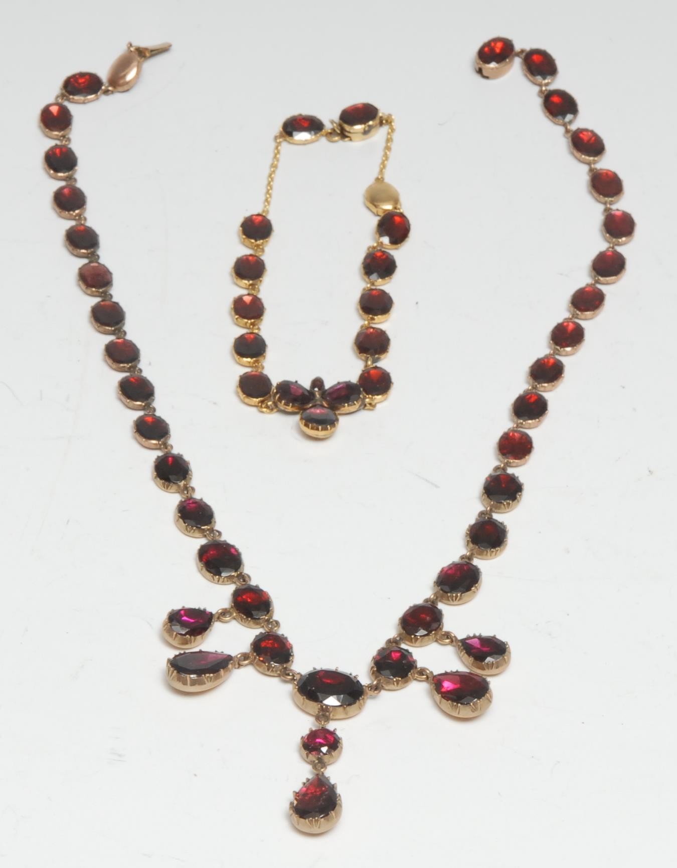 An Almandine garnet fringe necklace and bracelet suite,  composed of thirty five oval graduated almandine inset sections suspending five pear drop beads, mounted within an unmarked gold coloured metal frame, 40cm long;  similar seventeen stone bracelet, 17.5cm long, 30.8g gross