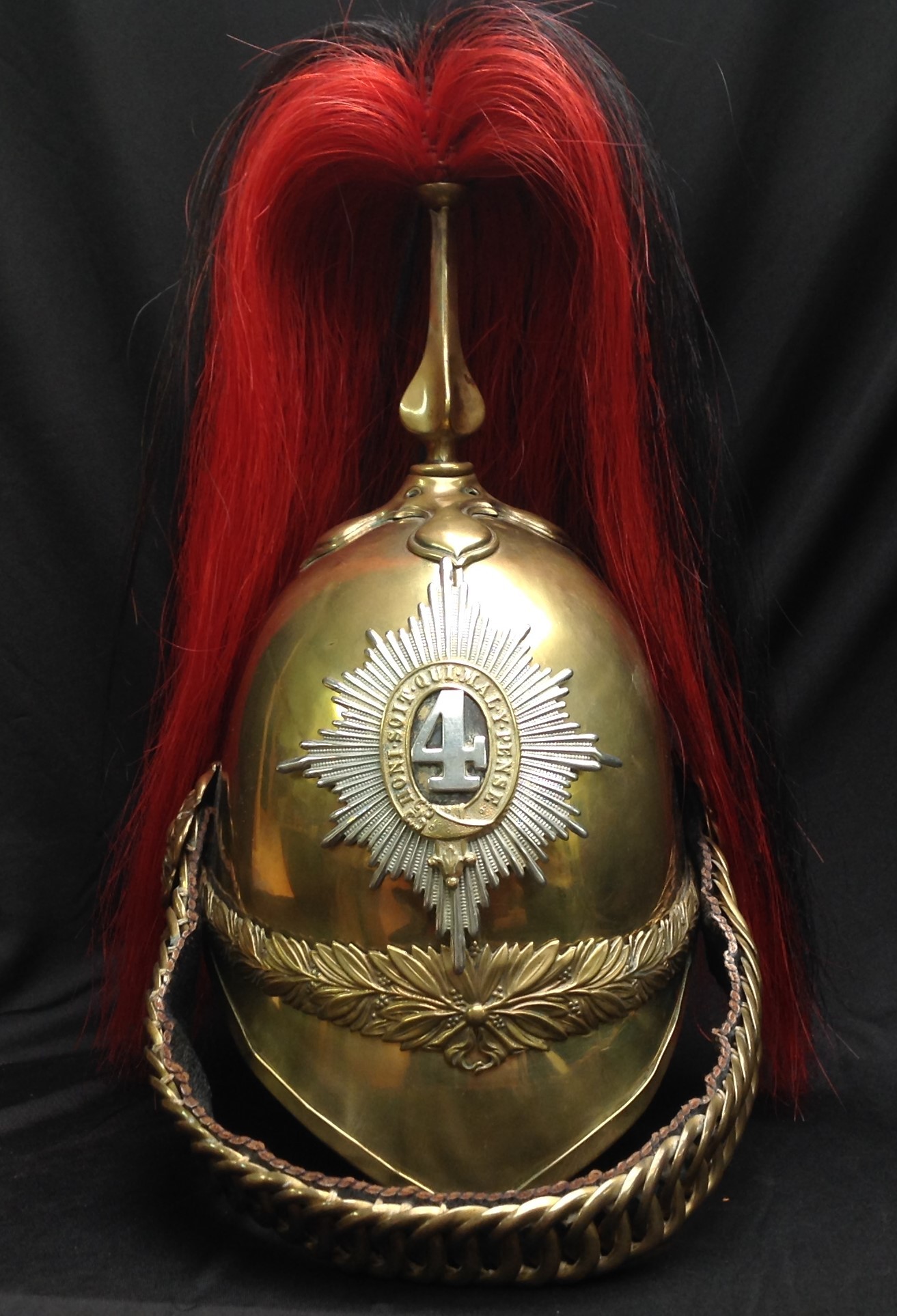 British Victorian 1871 Pattern Cavalry  Helmet. Brass skull with 4th Dragoon Guards regimental helmet plate to front. Helmet has brass cross base and fluted plume holder which houses a falling red/black horse hair plume. Rosette to top of holder. Copper rosettes which hold the chin chain backed with black leather. Dark brown leather liner. Underside of peak has a thin leather covering.