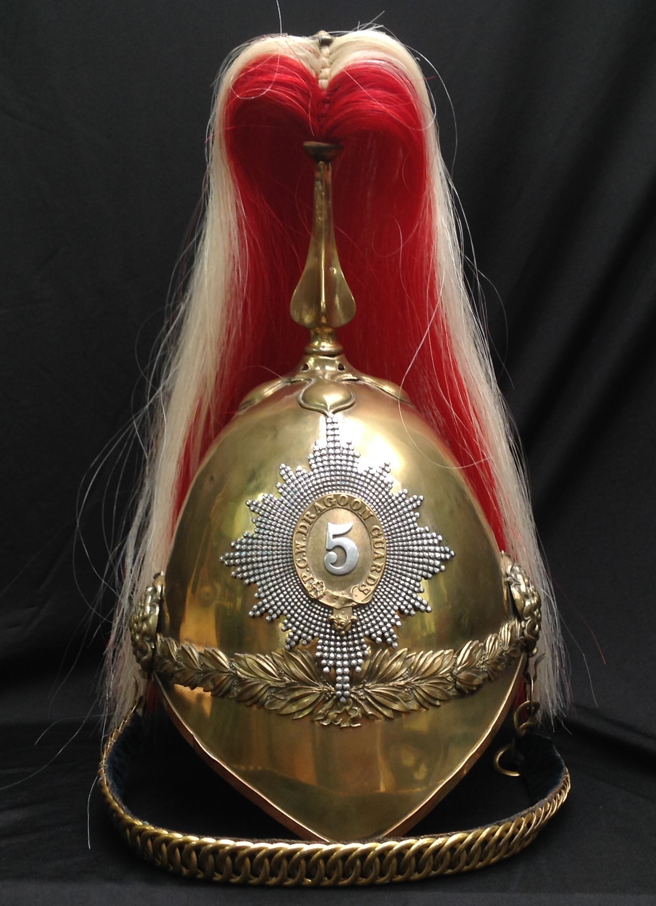 British Victorian 1871 Pattern Cavalry  Helmet. Brass skull with 5th Princess Charlotte of Wales Dragoon Guards regimental helmet plate to front with hobnail pattern star. Helmet has brass cross base and fluted plume holder which houses a falling red/white horse hair plume. Rosette to top of holder. Brass rosettes which hold the chin chain backed with black velvet. Underside of peak has remains of a  thin leather covering. Rear brim is leather covered. No liner or liner band.