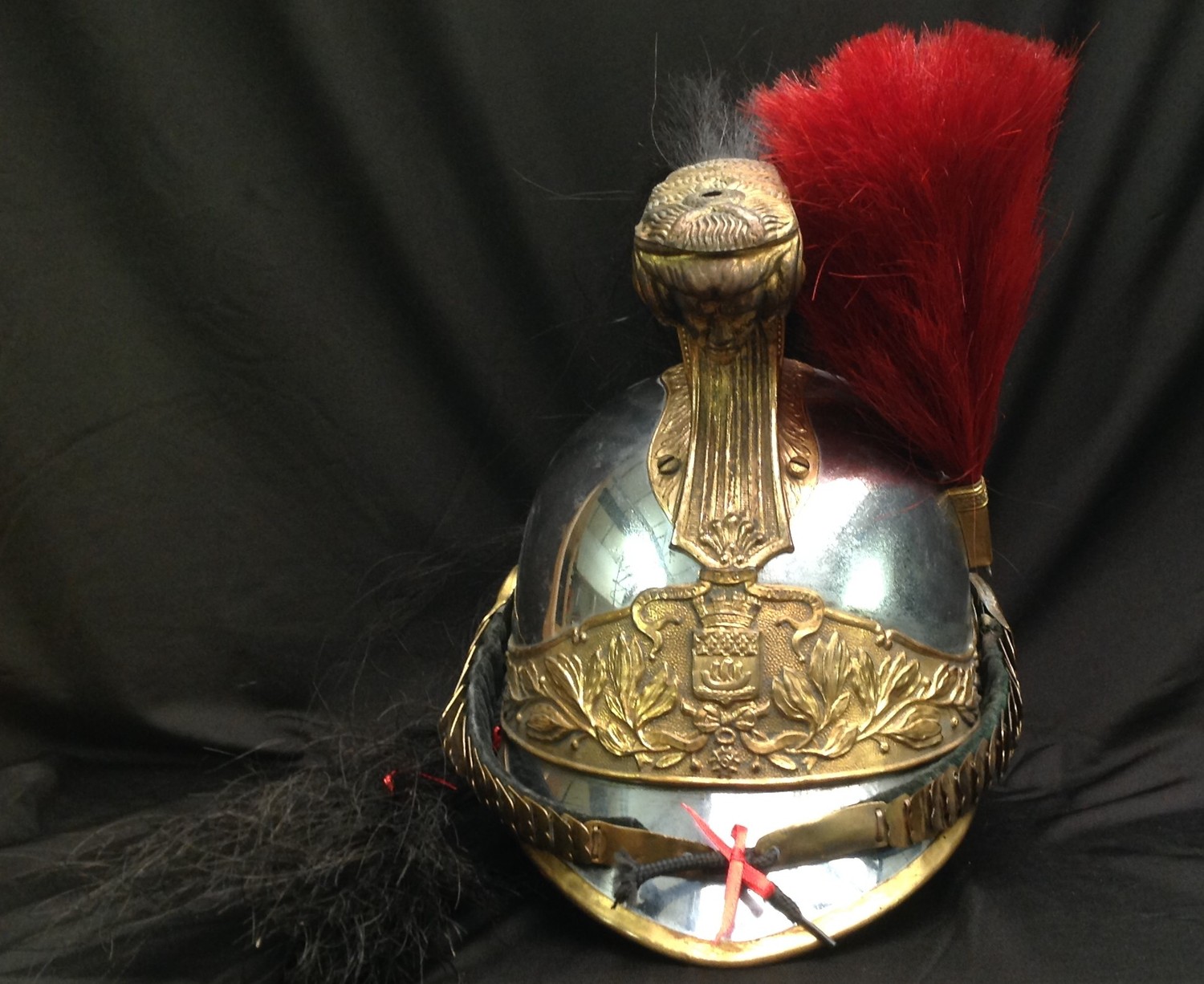French Republican Guard of the City of Paris Cuirassier helmet. Maker marked to rear of helmet "Siraudin & Hersant". Also stamped with various issue accountability numbers to the rear of the helmet body. The body is silvered metal with the edges banded in gilded brass. The gilded comb is decorated on both sides with volutes and laurel leaves and the front bears the head of Medusa. A black horsehair tail hangs from the rear of the comb. Slightly convex chinscales on a soft black velvet backing are attached to two large bosses. A gilded socket on the left side supports a small red horse hair plume. Seven-fingered brown leather liner. Front and rear peaks are lined with brown leather. Name scratched into the leather on the rear peak "Houdep".