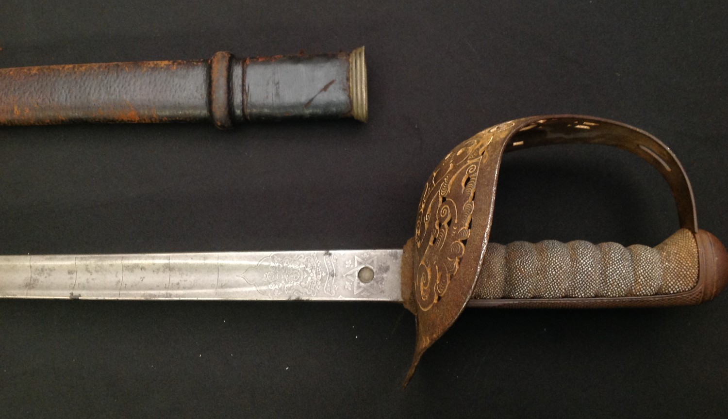 WW1 British 1897 pattern Officers Sword with single edged fullered blade 820mm in length. Proof marked. Maker marked "Henry Wilkinson, Pall Mall, London". Etched decoration to blade has 1 inch calibrations starting at 10 and ending at 36. Serial number to spine of blade 35967. Guard with GR V cypher. Shagreen grip, but missing grip wire. Overal length approx 985mm. Complete with leather covered scabbard.