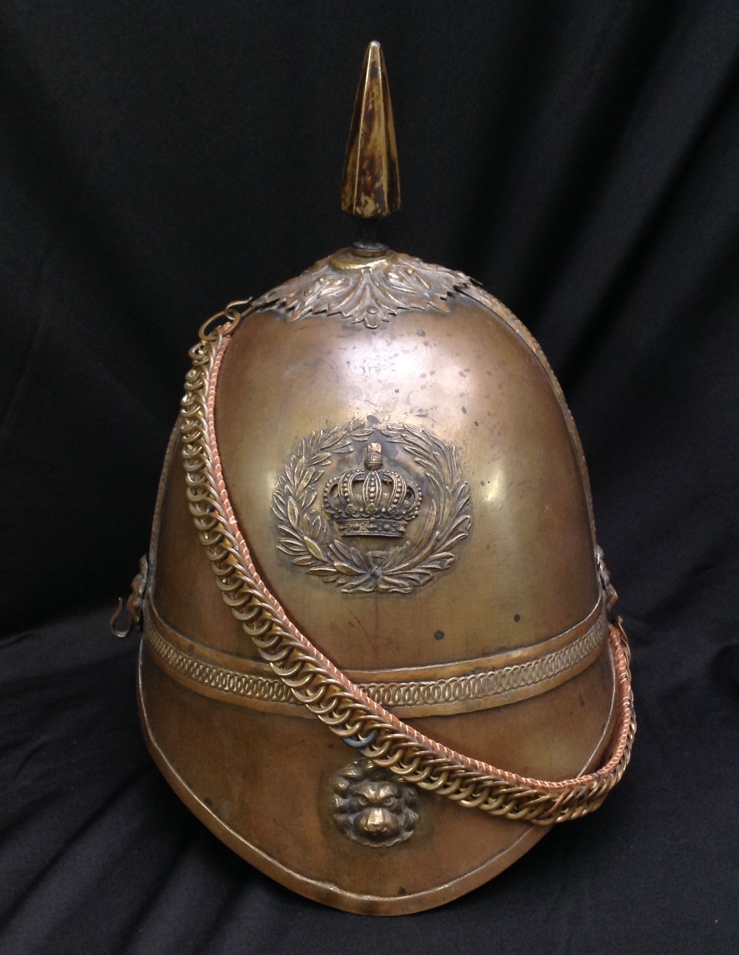 British Victorian 1st Yorkshires Other Ranks Helmet. Brass skull. Wreathed Queens Crown badge to front along with Lion's Mask to front peak. Spike to top on a leaf patterned base. Lion's mask mounts for chin chain. The chin chain is backed with brown leather. No liner or liner band. No leather to undersides of peaks. Uncleaned condition.
