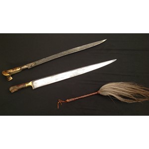 Pair of Indo-Persian Short Swords and a Horse hair fly swatter. First Sword has a ear style grip with single edged blade 530mm in length with gilt decoration. Horn grip. Some decoration missing from grip on one side. Overall length 675mm: the second sword has a single edged blade 542mm in length, wooden grip with some loss of wood to one side. Overall length 680mm. Neither swords has a scabbard; Fly swat is approx 560mm in overall length with leather bound grip, lanyard loop a/f (3)