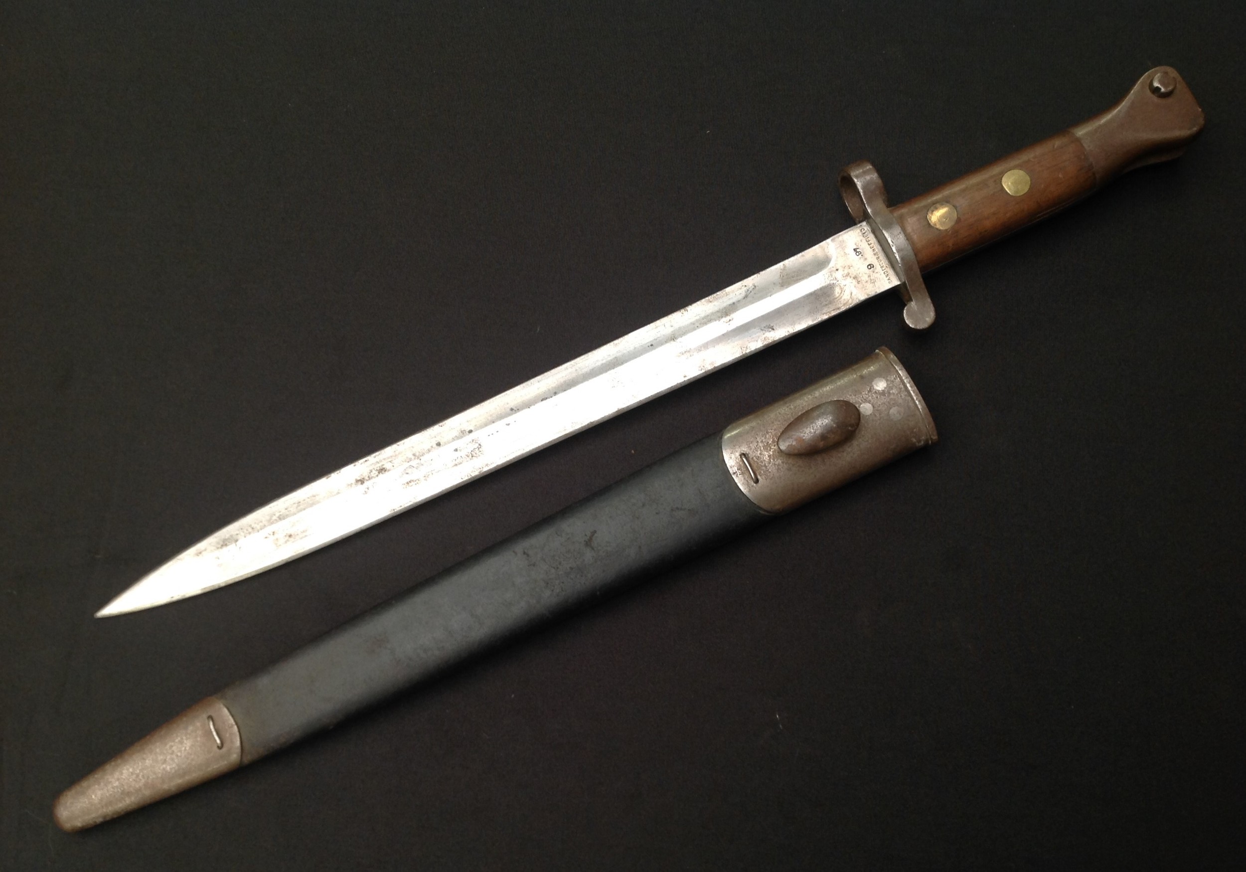 British 1888 pattern bayonet for Long Lee Enfield and Long Lee Metford rifles, 30cm blade by Sanderson, Sheffield, dated 9-97. Two-piece wooden grip. Pommel is regmentaly marked "9RS"  and  "986" Complete with steel-mounted leather scabbard, proof marks, plus "986" to throat of scabbard. 44cm long overall length.