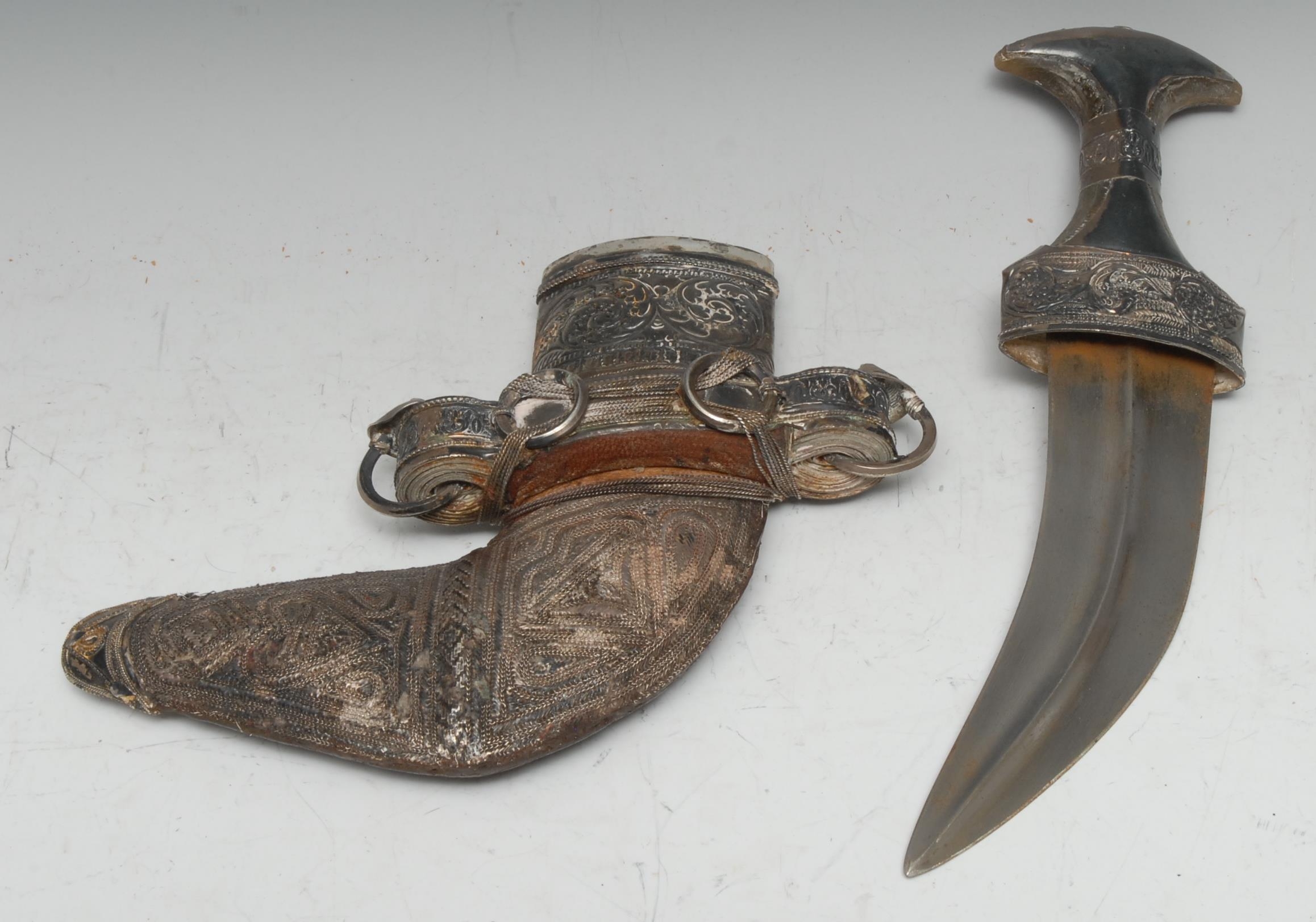 A Middle Eastern silver mounted jambiya, 17cm curved blade, horn grip, the hilt and scabbard applied with filigree and chased with scrolling foliage, 30cm long