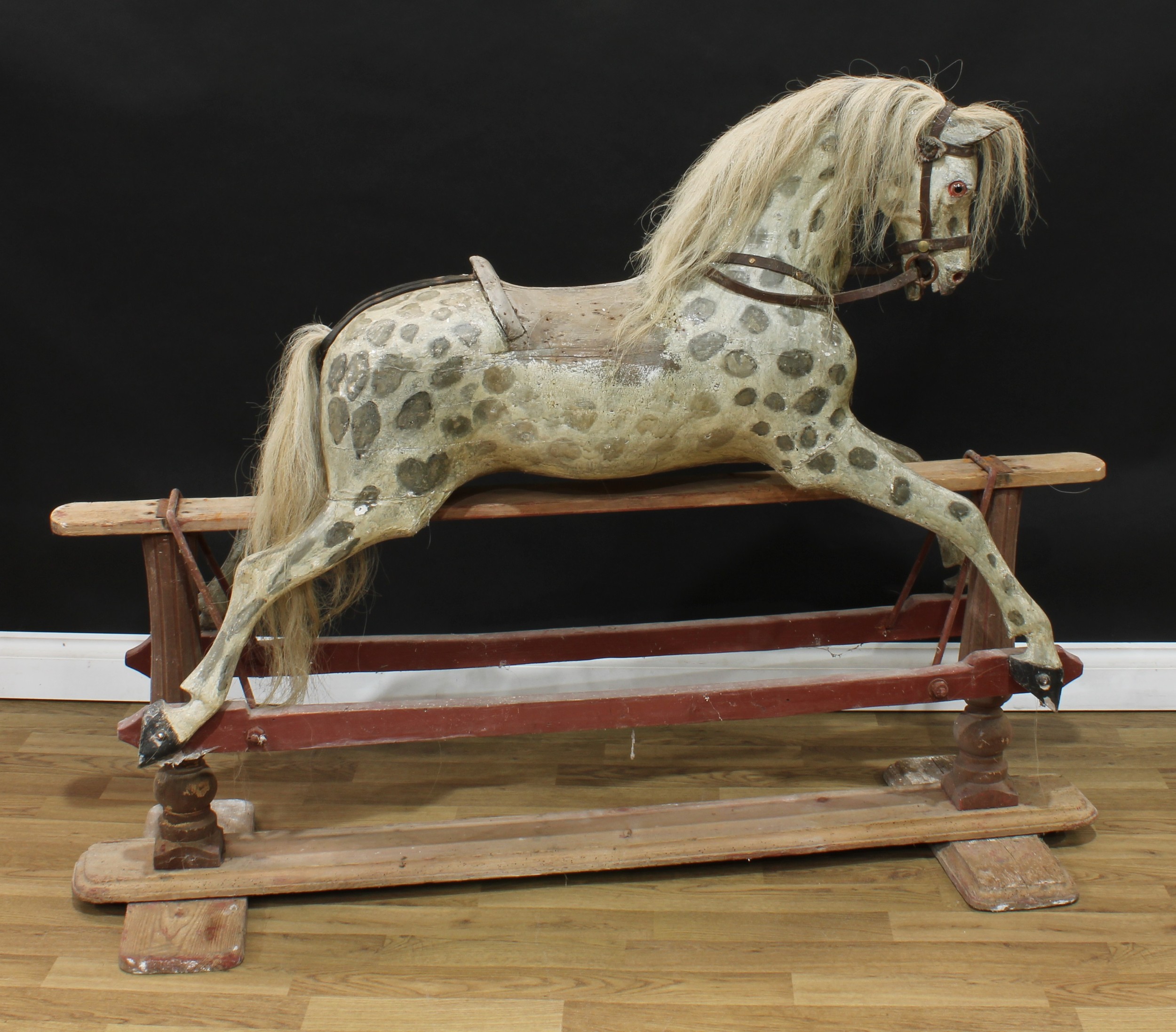 A large and substantial mid to late 19th century rocking horse on safety stand, attributed to Paul Leach, the finely carved, gesso and painted dappled horse with pricked ears, flared nostrils and open mouth revealing teeth, the sharply offset head with one clear and black glass eye, real horse hair mane and tail, the body with outstretched legs on a partially painted safety stand, 150cm long