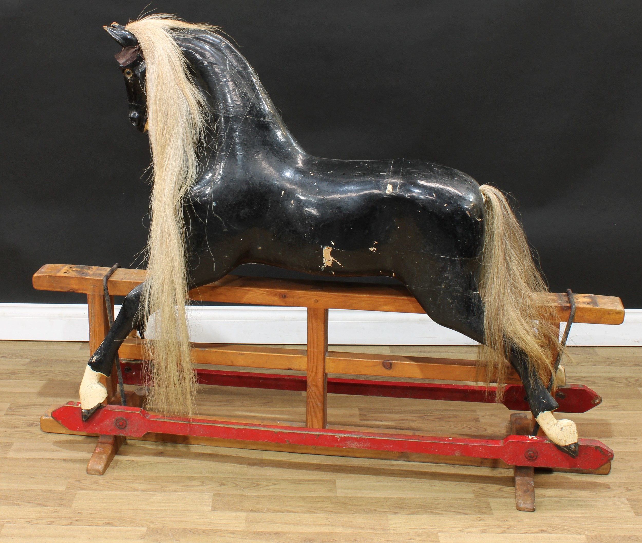 A large late 19th/early 20th century English rocking horse on safety stand, probably by F H Ayres, the black overpainted and carved rocking horse with pricked ears, flared nostrils and open mouth revealing teeth, the head with one clear and black glass eye, real horse hair mane and tail, the body with outstretched legs on a later replacement safety stand, remnants of the dappled paint can be seen, 152cm long