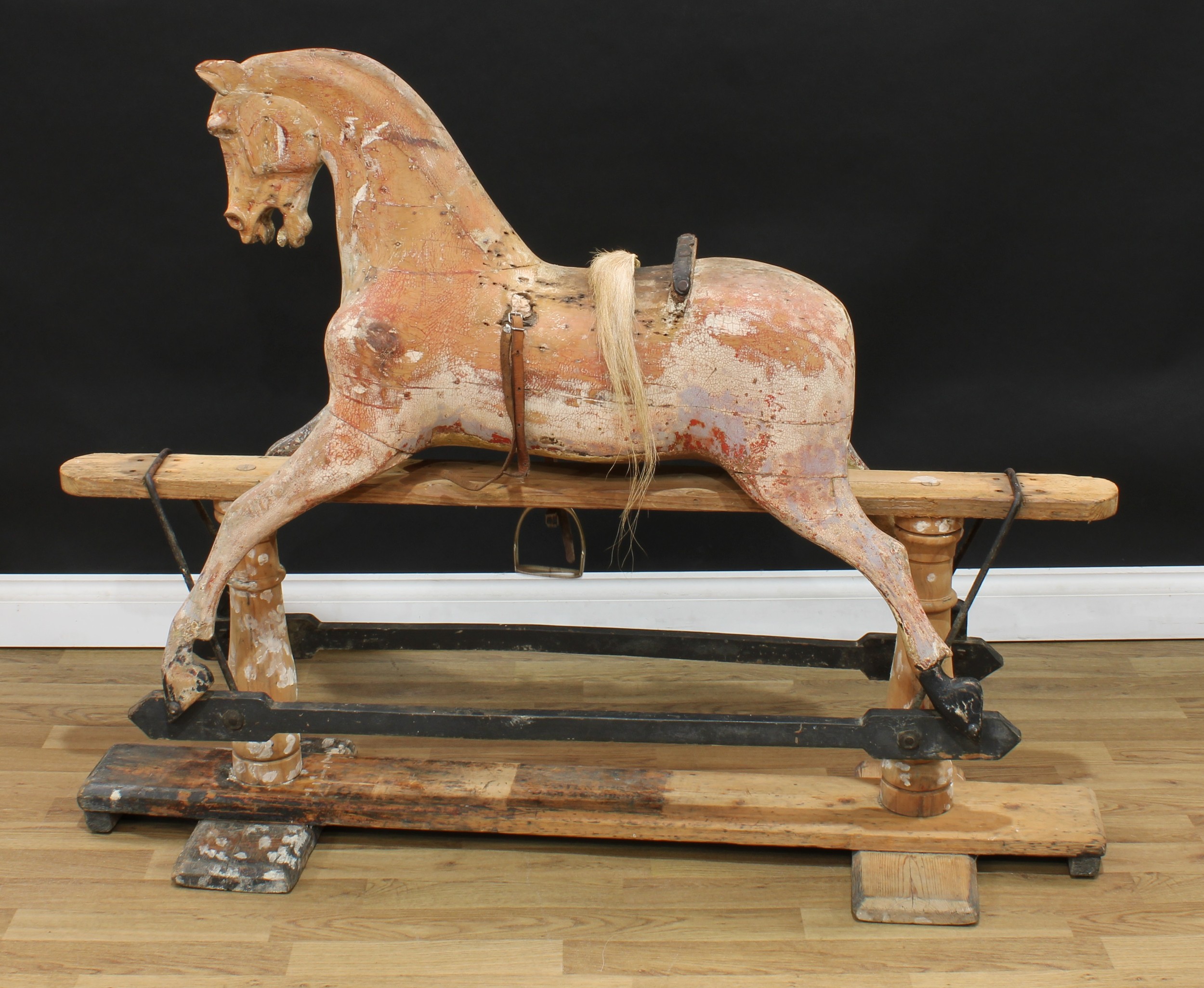 A late 19th/early 20th century English rocking horse on safety stand, probably by F H Ayres, the partially stripped and carved rocking horse with carved features, slightly offset head, the body with outstretched legs on an unassociated replacement stripped pine safety stand stamped 'PATENTED JAN 29TH 1880', the replacement stand probably by G & J Lines, 136cm long