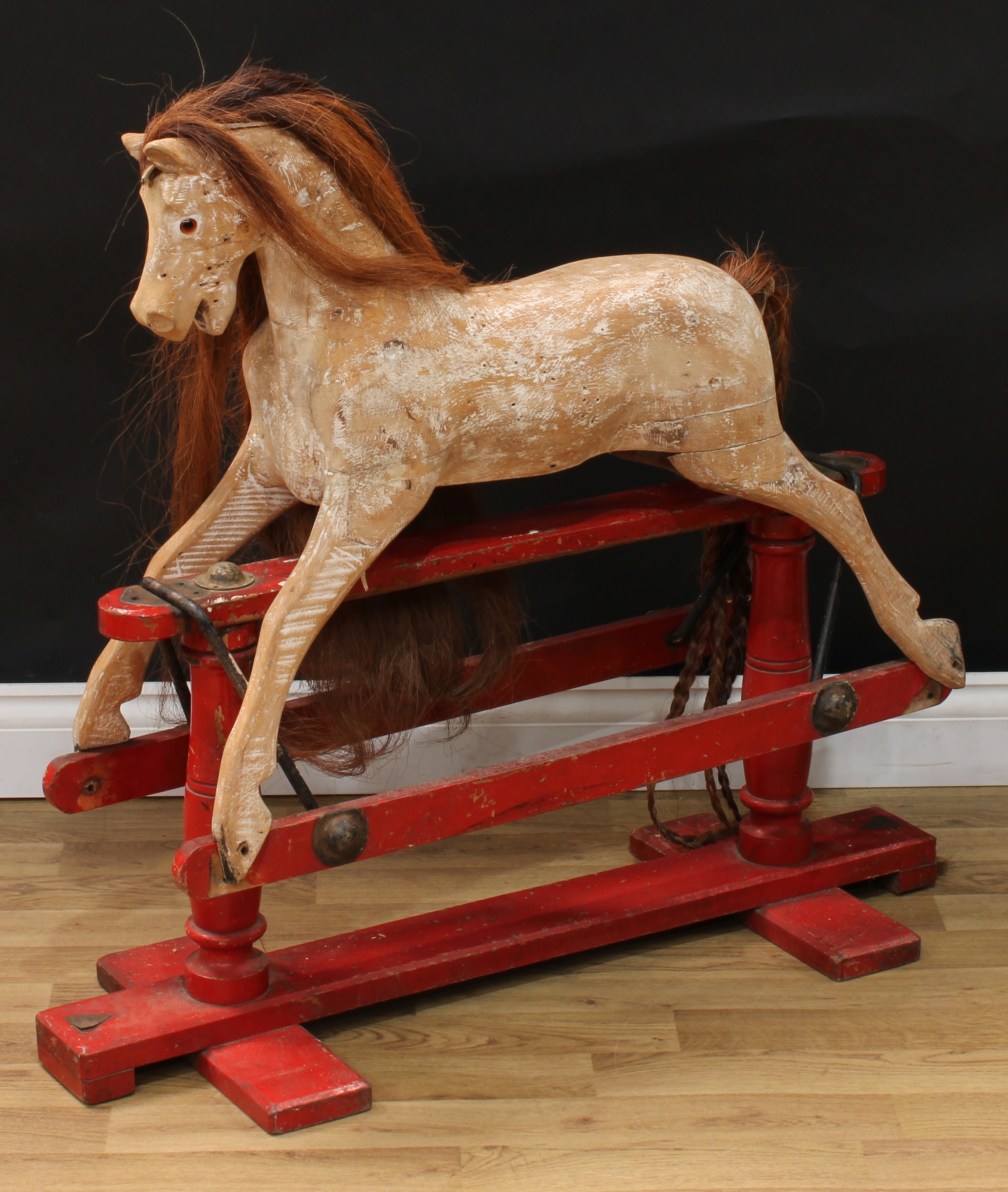 An early 20th century Lines Brothers rocking horse of small proportions, the stripped and carved wooden rocking horse with pricked ears, flared nostrils and open mouth, the head inset with amber and black glass eyes, real horse hair mane and tail, the body with outstretched legs on a painted red safety stand, trademark 'Lines Bros' red and black label to either end of base, 91cm long