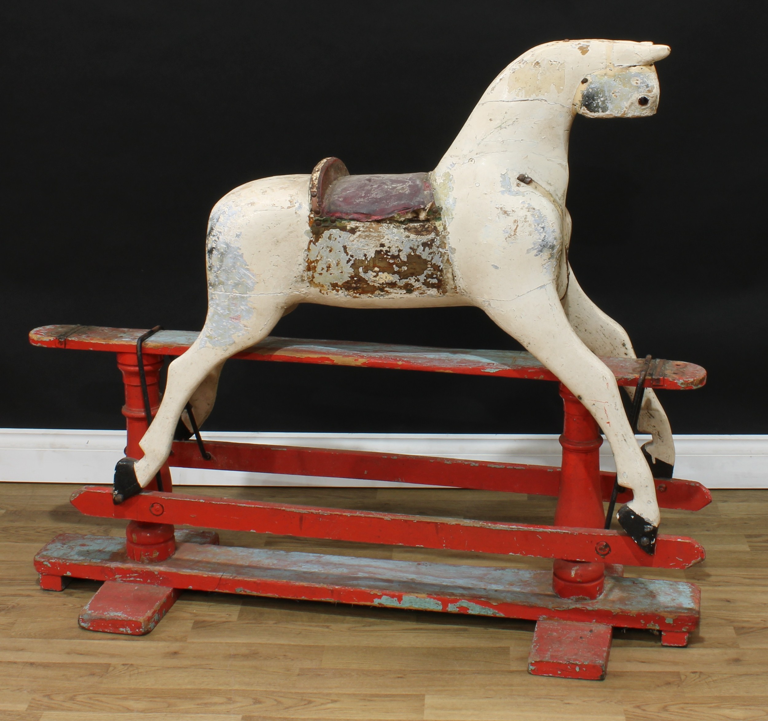 A late 19th/early 20th century English rocking horse on safety stand, the partially stripped and carved rocking horse with pricked ears and amber and black glass eyes, the body with outstretched legs on a painted safety stand, 128cm long