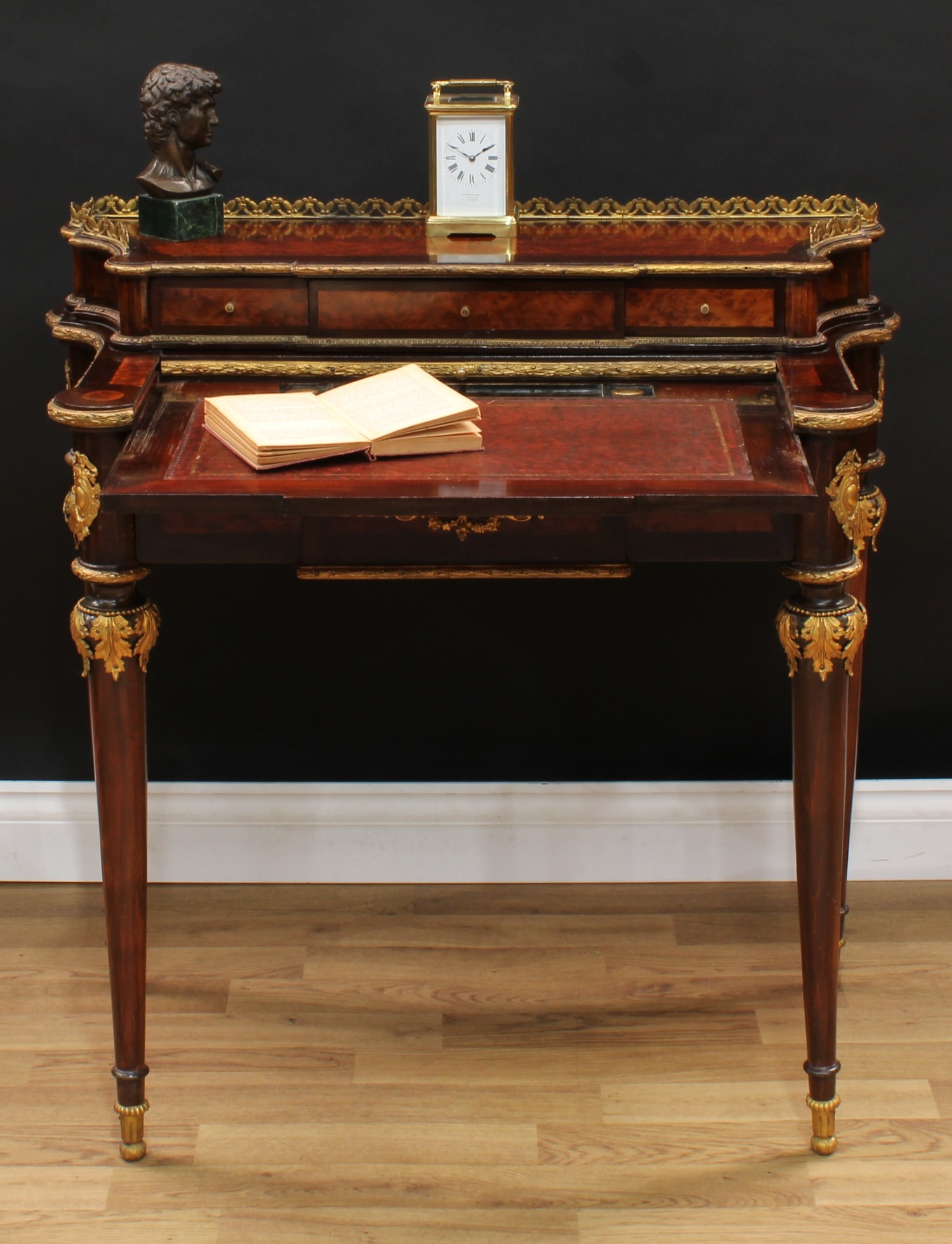 A Louis XV Revival gilt metal mounted bird's eye maple and mahogany writing table, of small and neat proportions, shaped superstructure with pierced fleur-de-lis gallery above three small drawers, the central sliding cover enclosing a retractable tooled and gilt writing surface and a pair of glass inkwells, above a frieze drawer, tapered cylindrical legs, 86cm high, 88cm wide, 47cm deep, c.1900