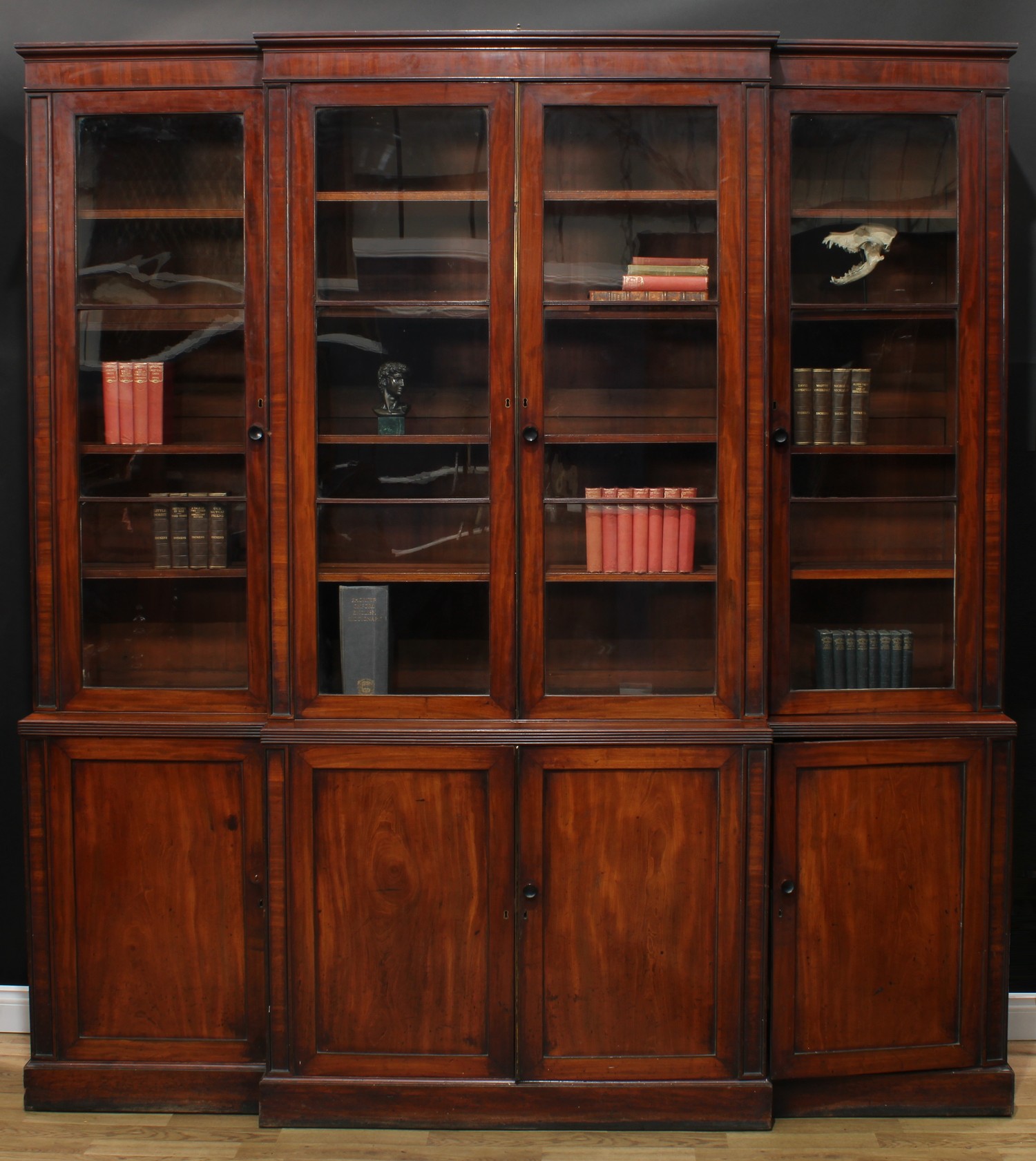 A Regency mahogany break-centre library bookcase, by M. Wilson, 68 Great Queen Street [London], stamped, shallow moulded cornice above four rectangular glazed doors enclosing adjustable shelves, the projecting base with reeded edge above four further panel doors, plinth foot, 246cm high, 224cm wide, 50cm deep, c.1820