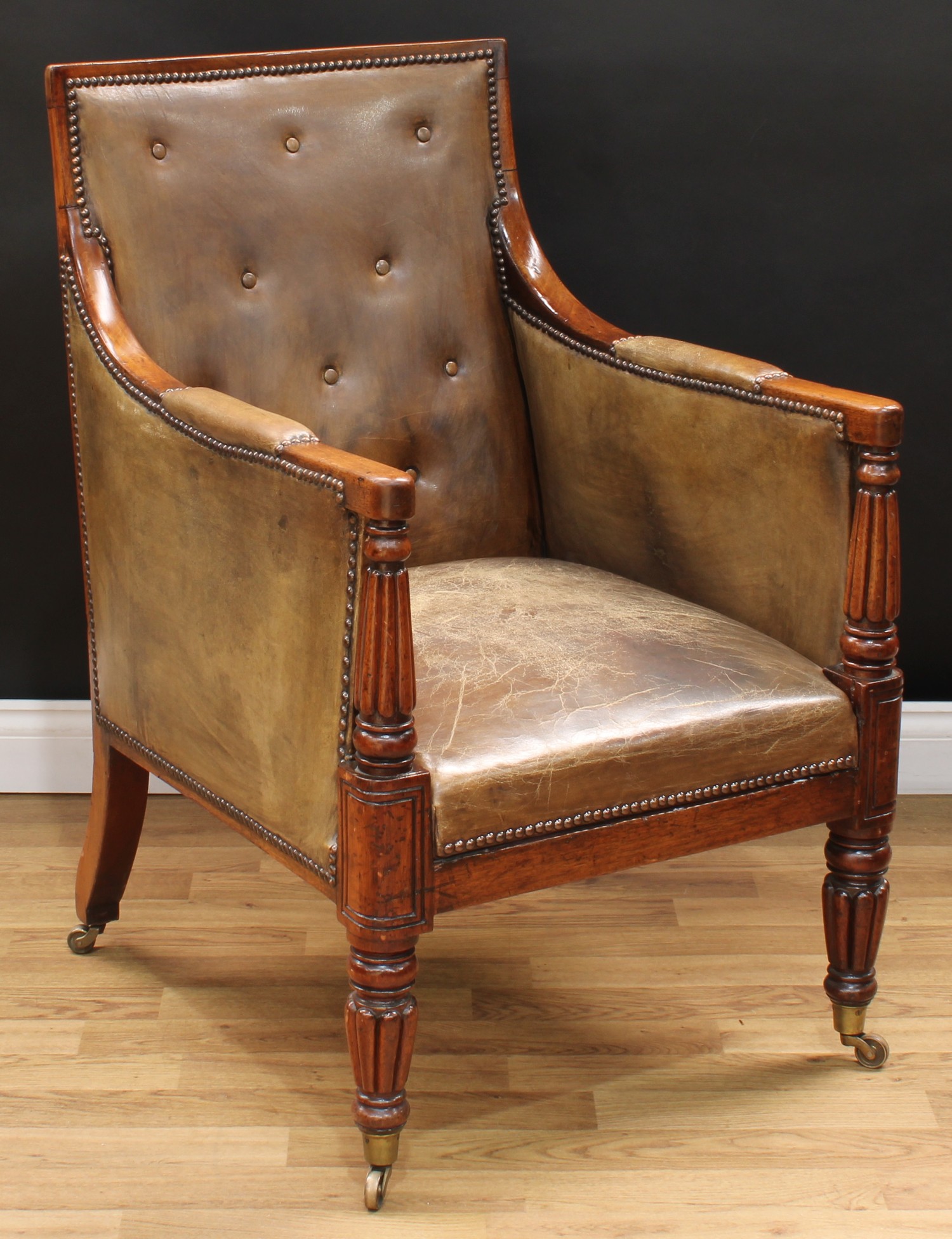 A George/William IV mahogany library chair, in the manner of Gillows of Lancaster, rectangular back, stuffed-over leather upholstery, turned and fluted arm supports and legs, brass casters, 98cm high, 59cm wide, the seat 57cm deep, c.1830