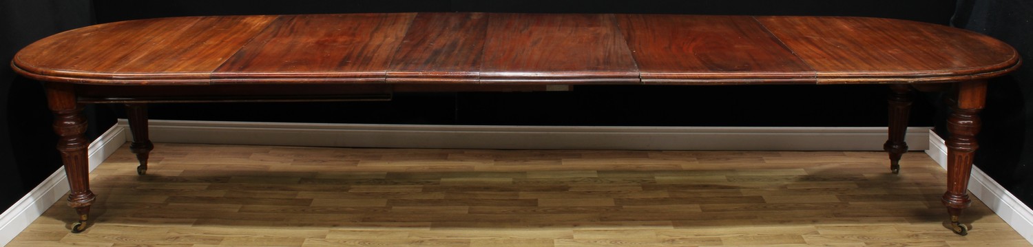 A large Victorian mahogany dining table, discorectangular top with moulded edge and four additional leaves, fluted tapered cylindrical legs, brass casters, 74cm high, 199.5cm opening to 420.5cm long, 110cm wide; leaf carrier en suite, 119cm high, 37.5cm, wide, 76cm deep, c.1880 (2)