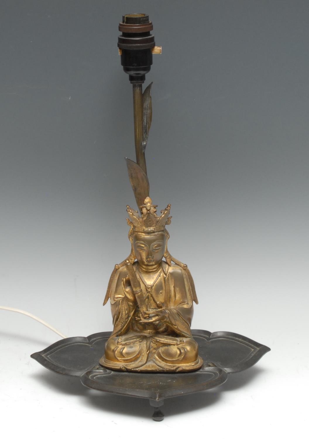 Chinese School (19th century), a gilt bronze, Boddhisatva, seated, holding a scroll, 16.5cm high, later mounted on a dark patinated bronze table lamp, as a lotus, 37.5cm high overall
