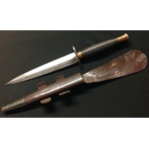 British Third Pattern Fairbairn Sykes Fighting Knife. 168mm long double edged blade with etched maker mark "Wilkinson Sword Ltd, Made in England". Crossguard unmarked. Cast alloy grip with copper undercoat finish showing, traces of the original black top coat finish remain to the grooves. Overall length 286mm. Complete with original scabbard with both leather tabs intact but missing elastic retaining loop. Blued steel chape.