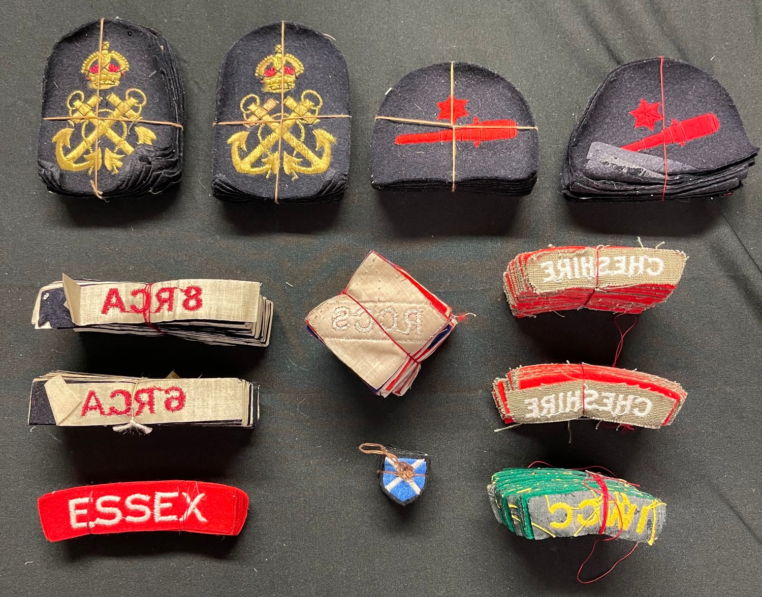 WW2 British and Canadian Army and Navy insignia, unissued still tied together with cotton. Essex Regt x 12, Cheshire Regt x 48, IWGC pre 1960 shoulder titles x 24, RN Petty Officers badges x 24, RN Trade badges x 24, 6 RCA, 8 RCA, etc.