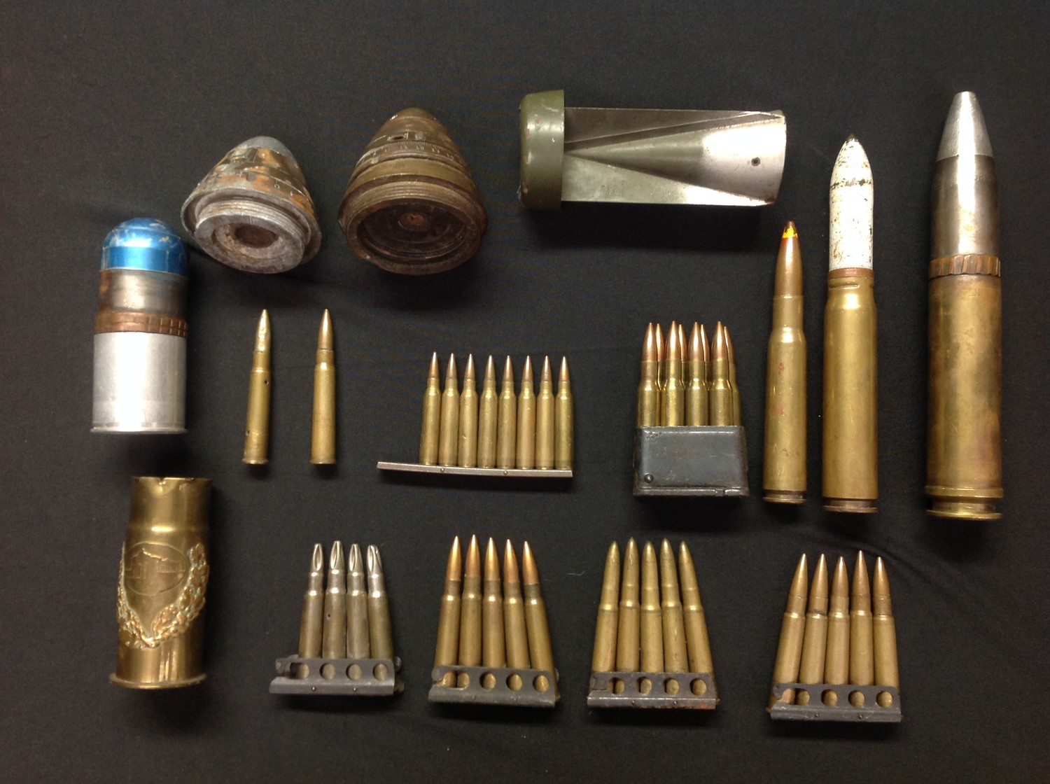 A collection of mixed assorted INERT FFE rounds, shell fuzes, etc. To include tail fin from a WW2 German incendiary bomb, US M1 Garand clip with various dated .30-06 rounds, two British fuses inc No80 V, clip of .233 rounds, clips of British .303 rounds, WW1 trench art German shell case, post war .50 cal round, post war 30mm Cannon round, post war 20mm cannon round, 40 x 46 Rifle Grenade, etc.