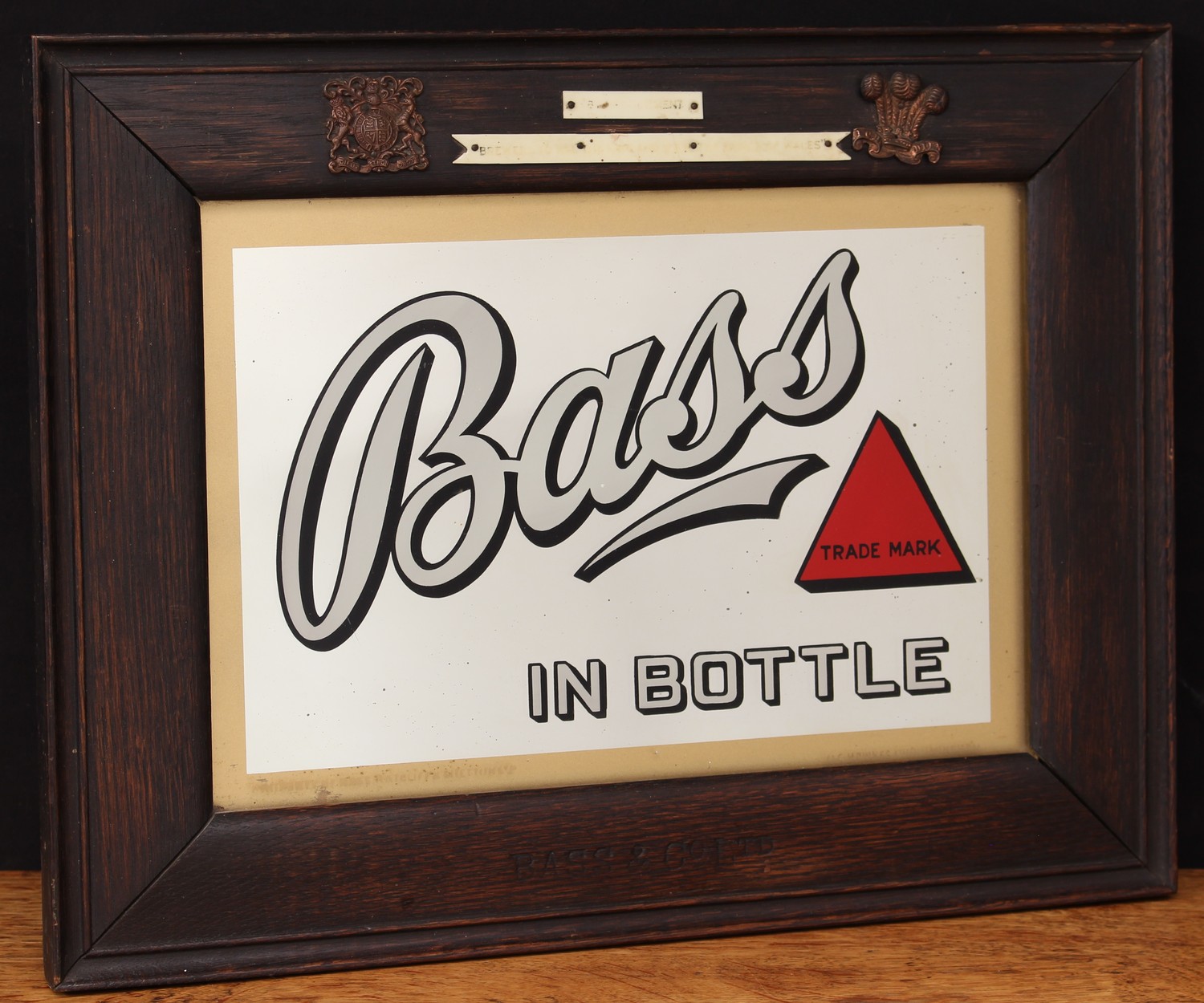 Advertising, Breweriana - an early 20th century Bass rectangular advertising point of sale pub/brewery mirror, "Bass IN BOTTLE", in black and white lettering with trademark red triangle logo, gilt border, framed, the lower edge border stamped 'BASS & CO LTD', the lower right corner of the glass etched with the makers mark for O.C. HAWKES BIRMINGHAM, 34cm x 44cm (measurements including frame)