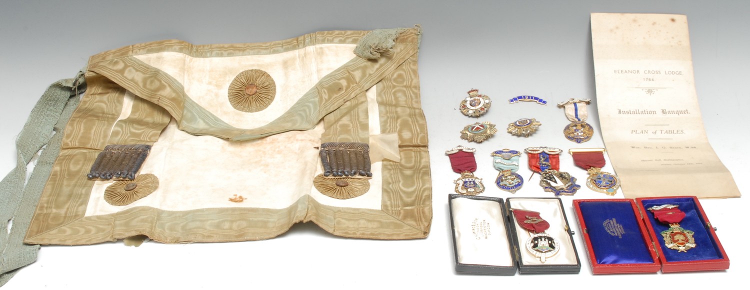 Friendly Society, Freemasonry - a collection of silver gilt and enamel Masonic medals and pin badges, 1907-1912, to include: Medal by Spencer & Co., London (Birmingham 1909) Royal Masonic Benevolent Institution (RMBI) Festival 1910 steward’s medal, maroon ribbon, bearing enamel shield of County of Essex, pin back, 8.3cm 12.7g in box of issue; Medal RMBI 1912 by George Kenning & Son (London 1911) arms of Guildford, plain suspense & pin back 8cm 18.3g in associated case; Medal RMBI by George Weeden & Co. London, (London 1906) arms of Rt. Hon. Sir Thomas Halsey, PC MP DL (1839-1927) impaling those of his wife Mary Julia Wells, red ribbon with central blue stripe, Steward Feby/1907 in enamel on suspense, pin back 410cm, 18.4g, *Sir Thomas was Conservative MP Herts 1874-1906 and was Deputy Grand Master of the Grand Lodge of England, Provincial GM for Herts and held numerous other freemasonic appointments; created baronet 1920, Medal RMBI 1907 by Henry Thomas Lamb & Co (HTL London 1907) coat of arms of Sir Augustus Webster of Copthall, Essex 7th Bt. pin back with maroon ribbon and gilt metal suspense 9cm 24.7g, *Sir Augustus Webster, 8th Bt (1864-1923) was seated at Battle Abbey and succeeded his father in 1886. His freemasonic connections are not known; Medal RMBI steward’s 1911 by George Weeden (London 1910) coat of arms of the David/Davie family, maroon ribbon suspense with enamel: Steward/Coronation/year, 9.3cm, 13.1g; Medal Royal Masonic Institution for Boys, by George Spencer & Co of London (Birmingham 1910) earl’s coronet over arms of the Earl of Radnor, ‘steward’ to ribbon suspense enamelled Coronation Year above the arms of Aske, pin back 9cm, 18.6g, * Jacob Pleydell-Bouverie, 6th Earl of Radnor CIE, CBE (1868-1939 was MP (Con) Wilton 1892-1900 when he succeeded to the earldom; served WW1 Col. (later Brigadier) 4th Bn. Wiltshire Regt. Chairman Royal Commission on the Care for the Feeble Minded, later Director of Agricultural Production 1918-1919, Lord Lieutenant of Wiltshire 1925-1930. His Freemasonic connections are unclear; Medal Royal Masonic Institute for Girls 1911 by George Weeden (London 1910) bearing the earls coronet and arms of Edmond, 7th Earl of Orkney, white ribbon with blue stripe, steward/Coronation/Year enamelled on suspense 9cm, 12.7gross, *Edmond FitzMaurice, 7th Earl of Orkney (of the 3rd [1696] creation) JP DL (1867-1951) succeeded in 1889 and was Col. 3rd Oxfordshire Light Infantry in WW1; he was famous for having married in 1892 Connie Gilchrist, ‘The original Gaiety Girl’. His freemasonic connections are not known; Badge, pin backed, by Spencer & Co. (Birmingham 1909) bearing an earl’s coronet ensigning the arms of the Earl of Euston within a collar of acanthus, ‘Mark Benev[o]l[ent] Fund 1910’ 4.5cm dia.,12.9g, *Henry FitzRoy, Earl of Euston (1846-1912) JP DL was the eldest son and heir of 7th Duke of Grafton, who outlived him. He was Col. Cmdt. 1st Vol. Bn. Northamptonshire Regiment later Hon. Col. 5th Bn. His freemasonic connections are not known; Badge, pin backed, by Spencer & Co. (Birmingham 1908) consisting of a nailhead and rayonné 16 point gilt star bearing the arms of Curry, on the garter ‘Mark Benevolent Fund 1909’ 4.5cm dia., 18.4g; Badge, pin backed by Spencer (Birmingham 1910) 14 point star of acanthus and fleurs-de-lys, arms of Heneage, on garter ‘Mark Benevolent Fund 1911’4cm dia, 19.8g; Badge, silver gilt and enamel ribbon 1911 on blue enamel Spencer London (Birmingham 1911) 4.5cm long, 2.7g; Also 27.5 x 33cm card seating plan and name index for the installation banquet, Eleanor Cross Lodge, Northampton held 14th October 1910, a Masonic apron in white chamois leather edged green watered silk, gilt tassellage, some of these medals/badges bear arms associated with Northamptonshire, eg Lord Orkney and the Heneages (collection)