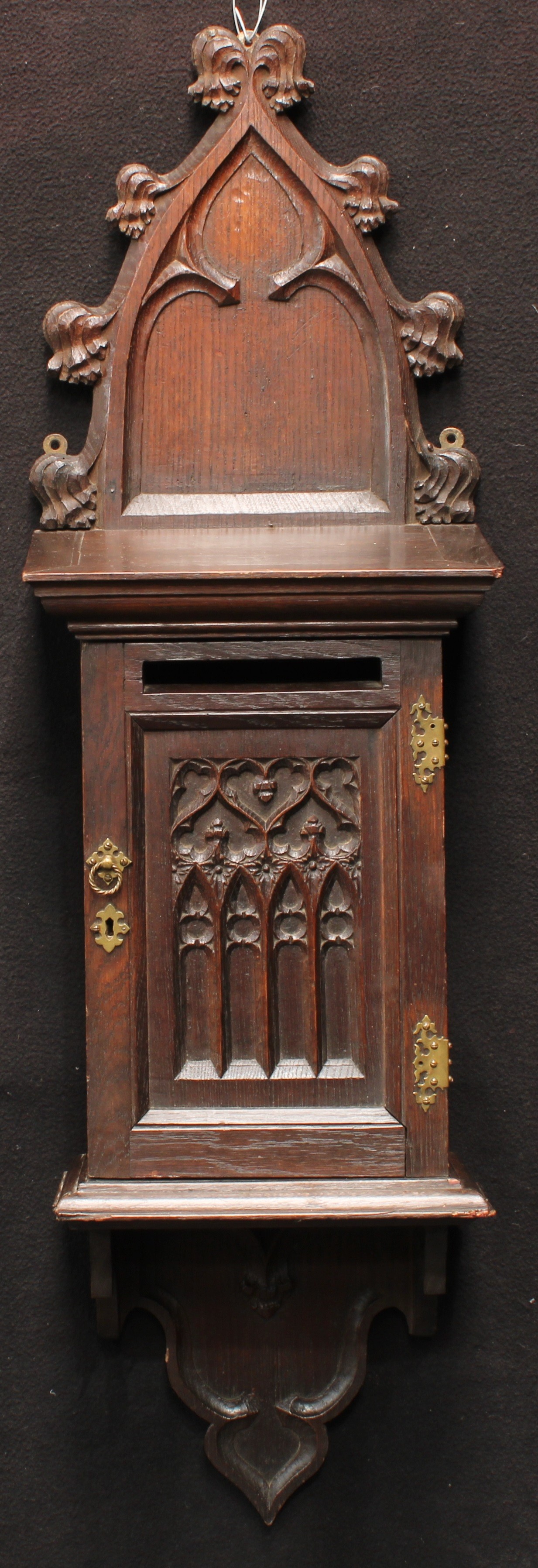 A 19th century Gothic Revival oak wall mounted country house post box, shaped cresting, moulded cornice above a rectangular door with letter aperture and carved blind tracery panel, 105cm high, 31cm wide, c.1880