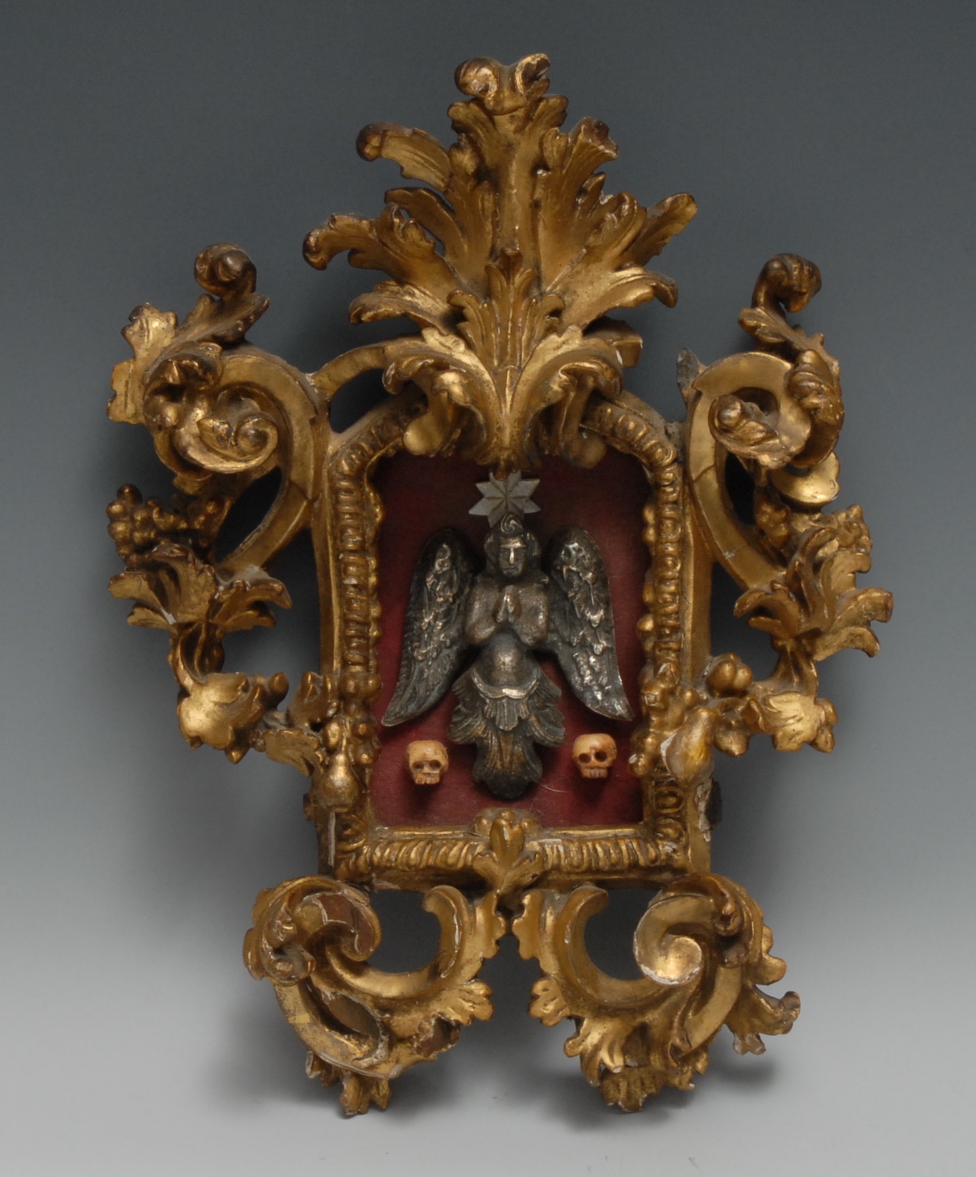 An 18th century Continental giltwood cartouche shaped frame, enclosing a momento mori tableau, 31cm high, 23cm wide