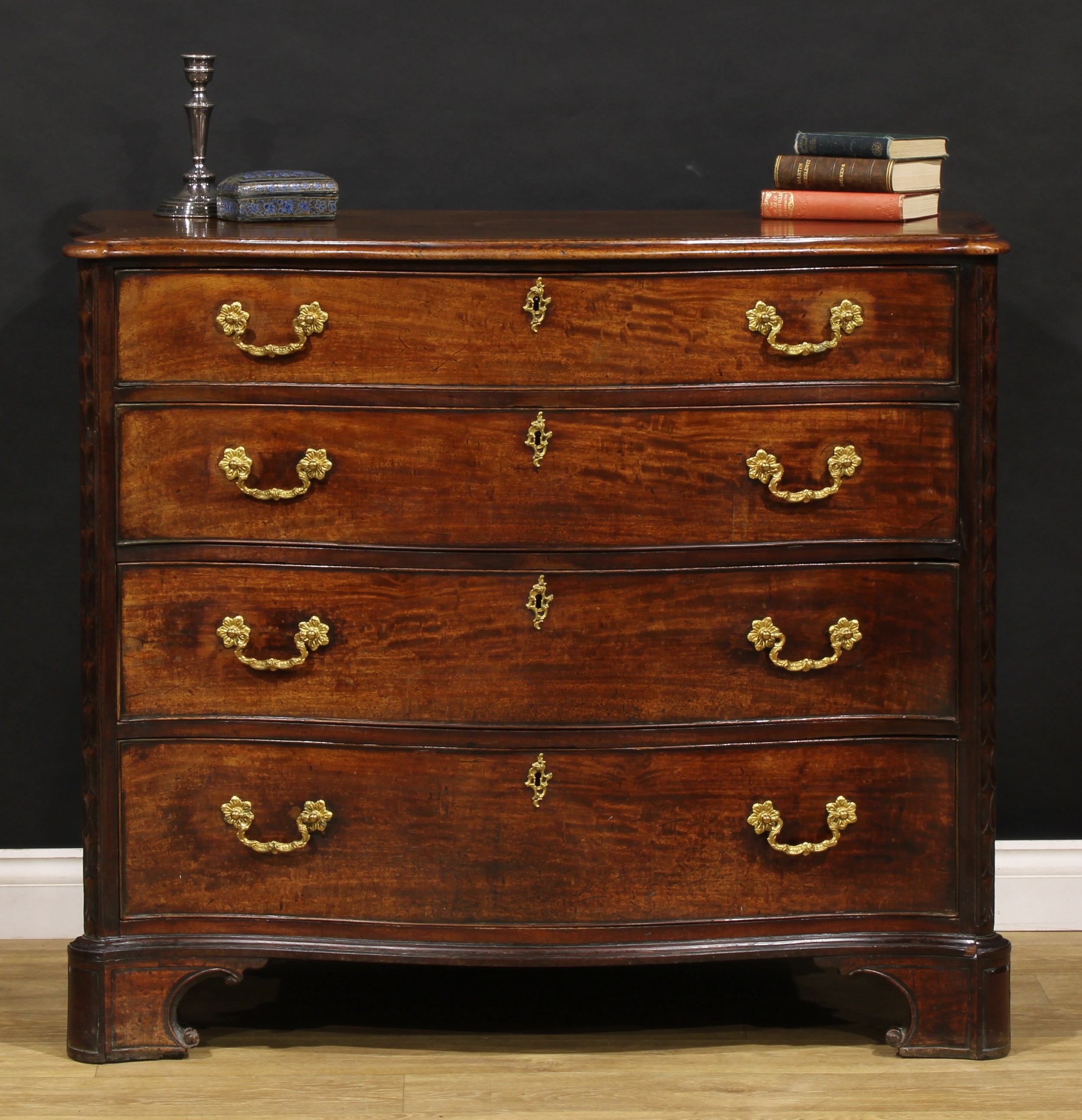 A George III mahogany serpentine chest, slightly oversailing top with moulded edge above four long cockbeaded drawers, flanked by carved canted foreangles, carry handles to sides, bracket feet, 98cm high, 117cm wide, 60.5cm deep, c.1780