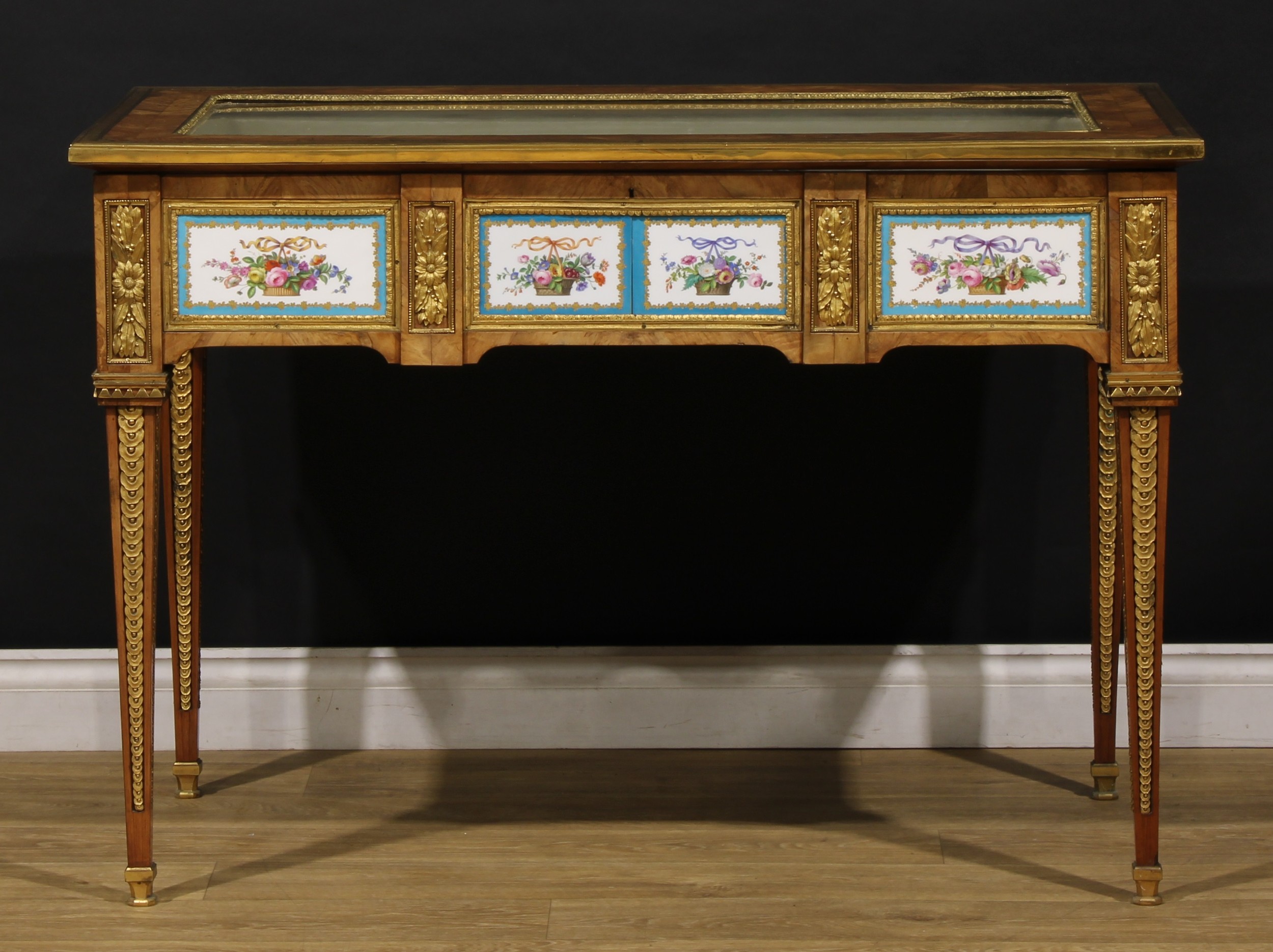 A Victorian Franglais gilt metal and porcelain mounted bijouterie table, hinged top, the porcelain mounts decorated in the manner of Sèvres with ribbon-tied baskets of flowers within a bleu celeste border, tapered square legs, the lock stamped NETTLEFOLD PATENT, beneath a crowned VR, 80cm high, 115cm wide, 63.5cm deep, c.1870