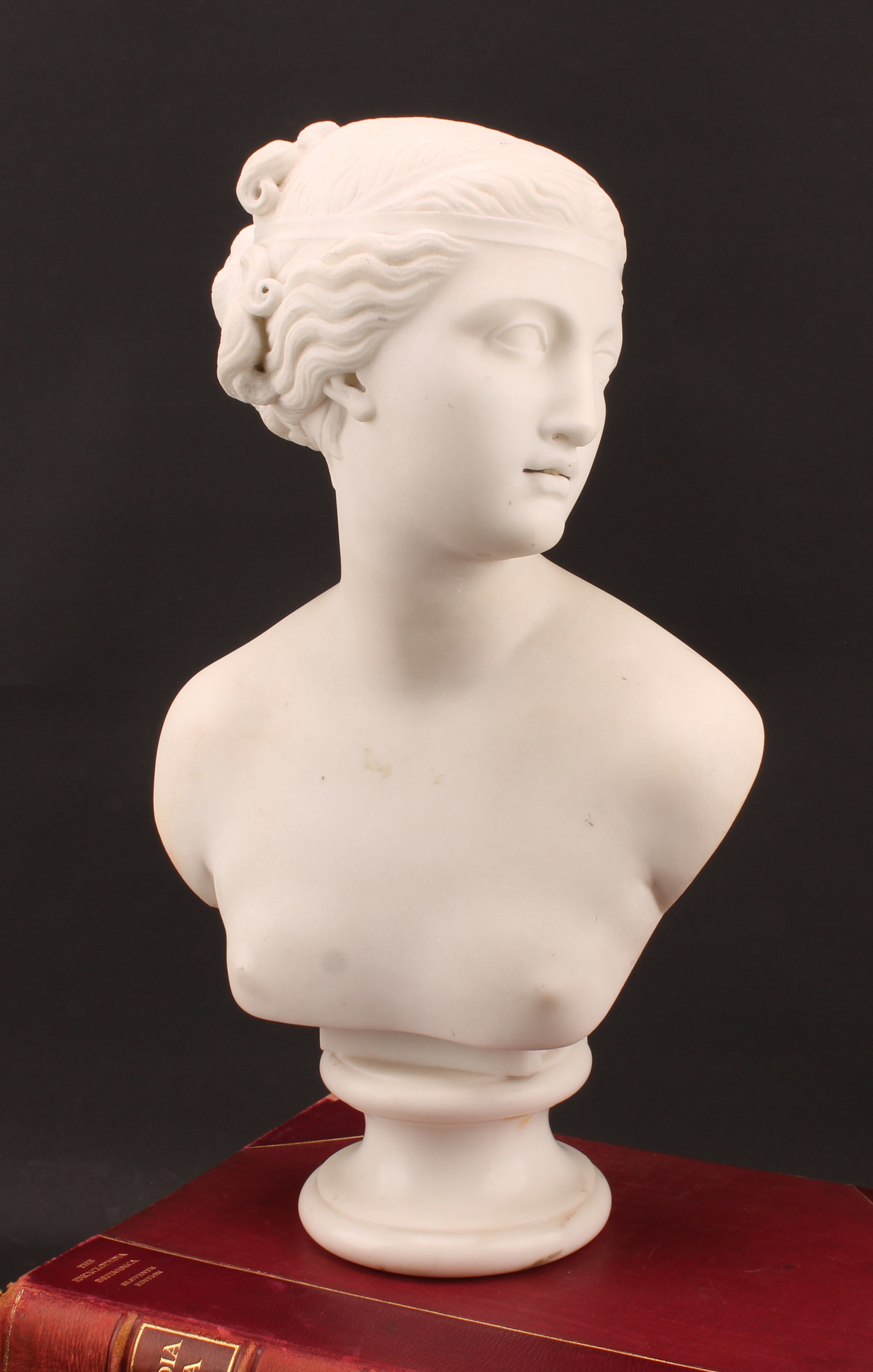 A mid 19th century marble portrait bust, in the style of William Calder Marshall, as a naked maiden, head turned to sinister, her hair held in ribbon lattice, circular socle plinth, unsigned, 40.4cm high, provenance The Earl of Faversham