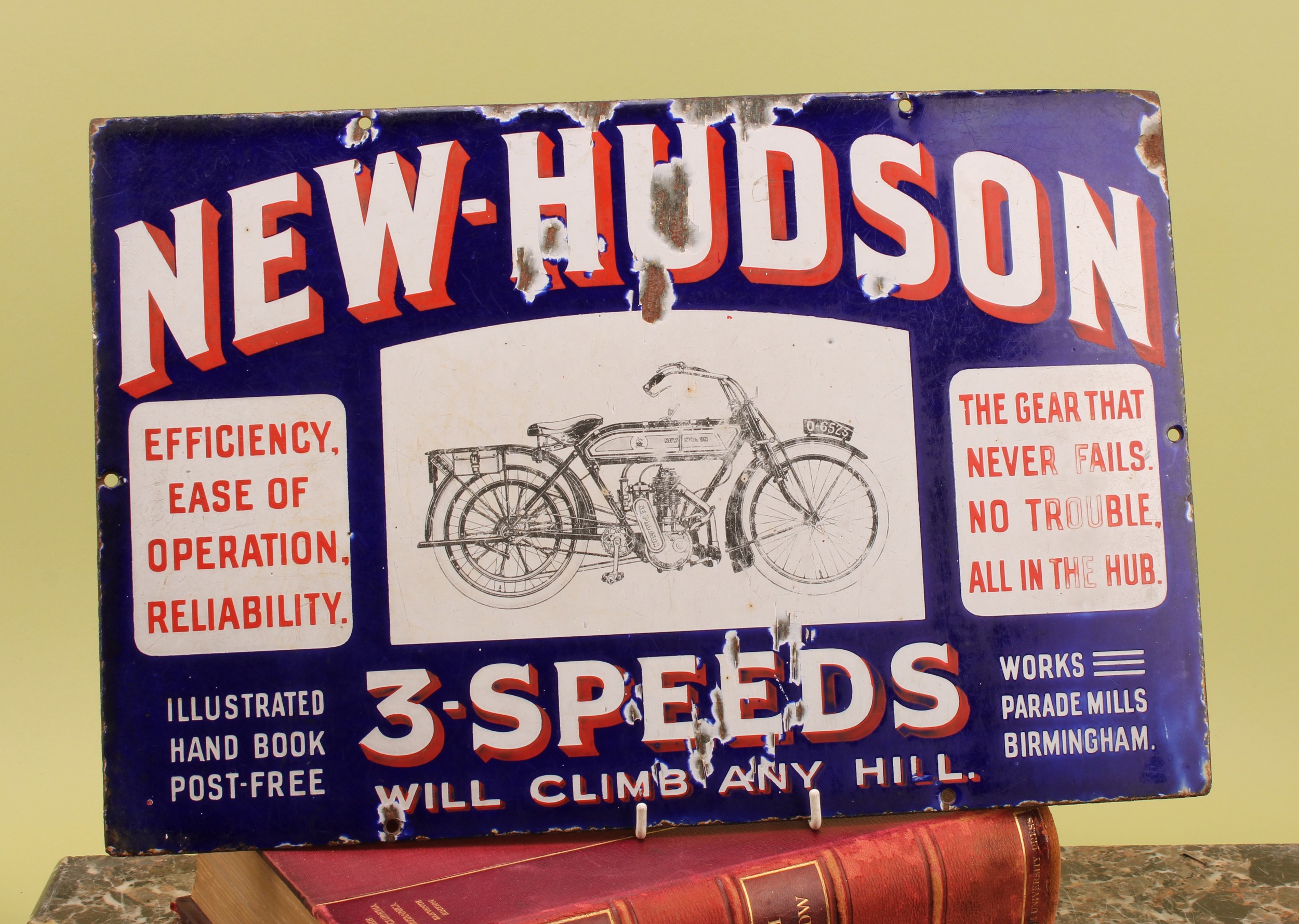 Advertising - motorcycling interest - a rectangular pictorial enamel sign, 'NEW-HUDSON 3-SPEEDS WILL CLIMB ANY HILL', red and white lettering on a blue ground, the central panel pictured in black with a New-Hudson motorcycle, 30.5cm x 46cm, early 20th century