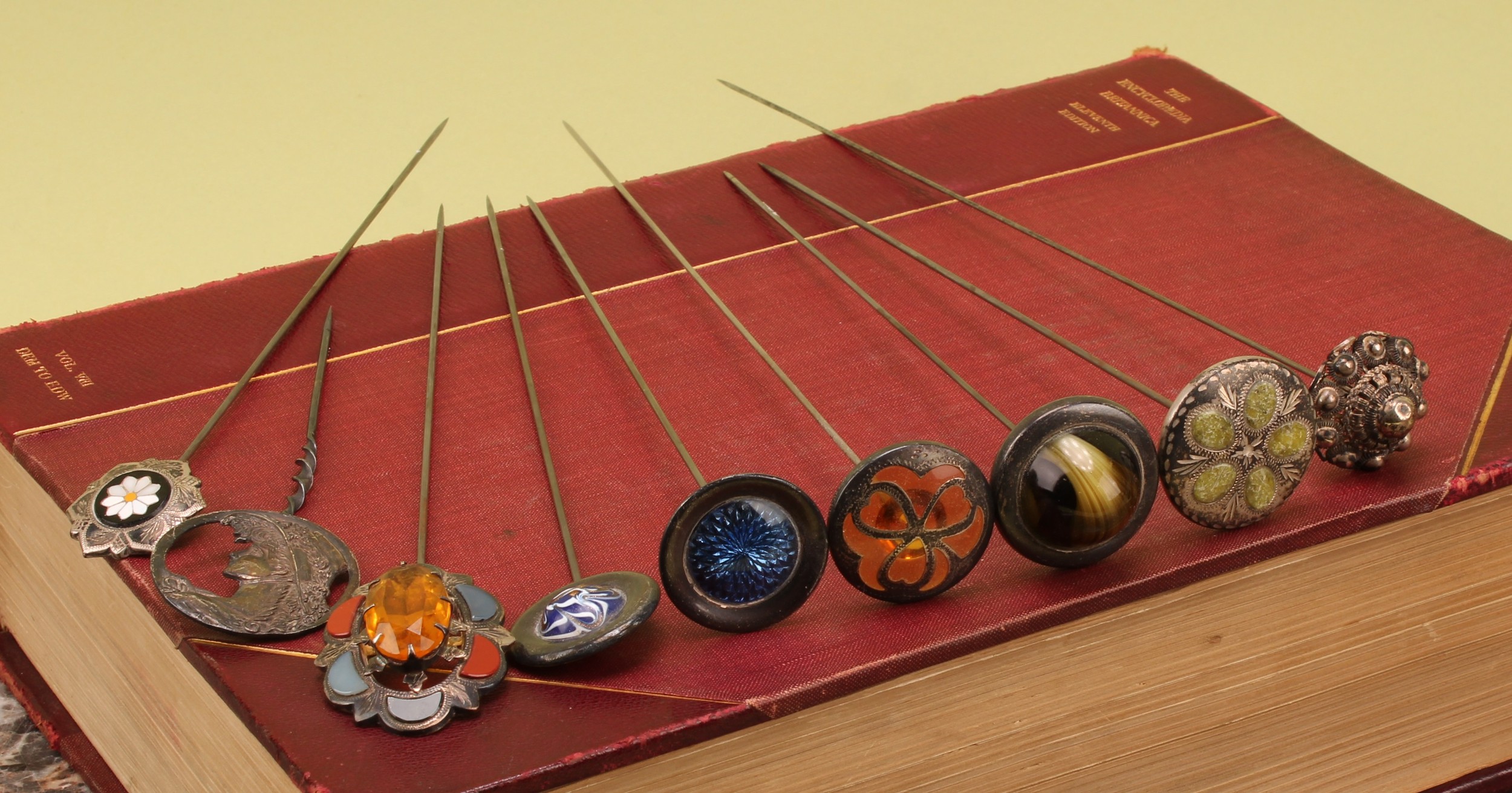 A collection of nine silver topped hat pins, early 20th century and later, including Art Nouveau swivel top, enamel swivel top, filigree, glass set, Scottish style, etc, the longest 27cm (9)