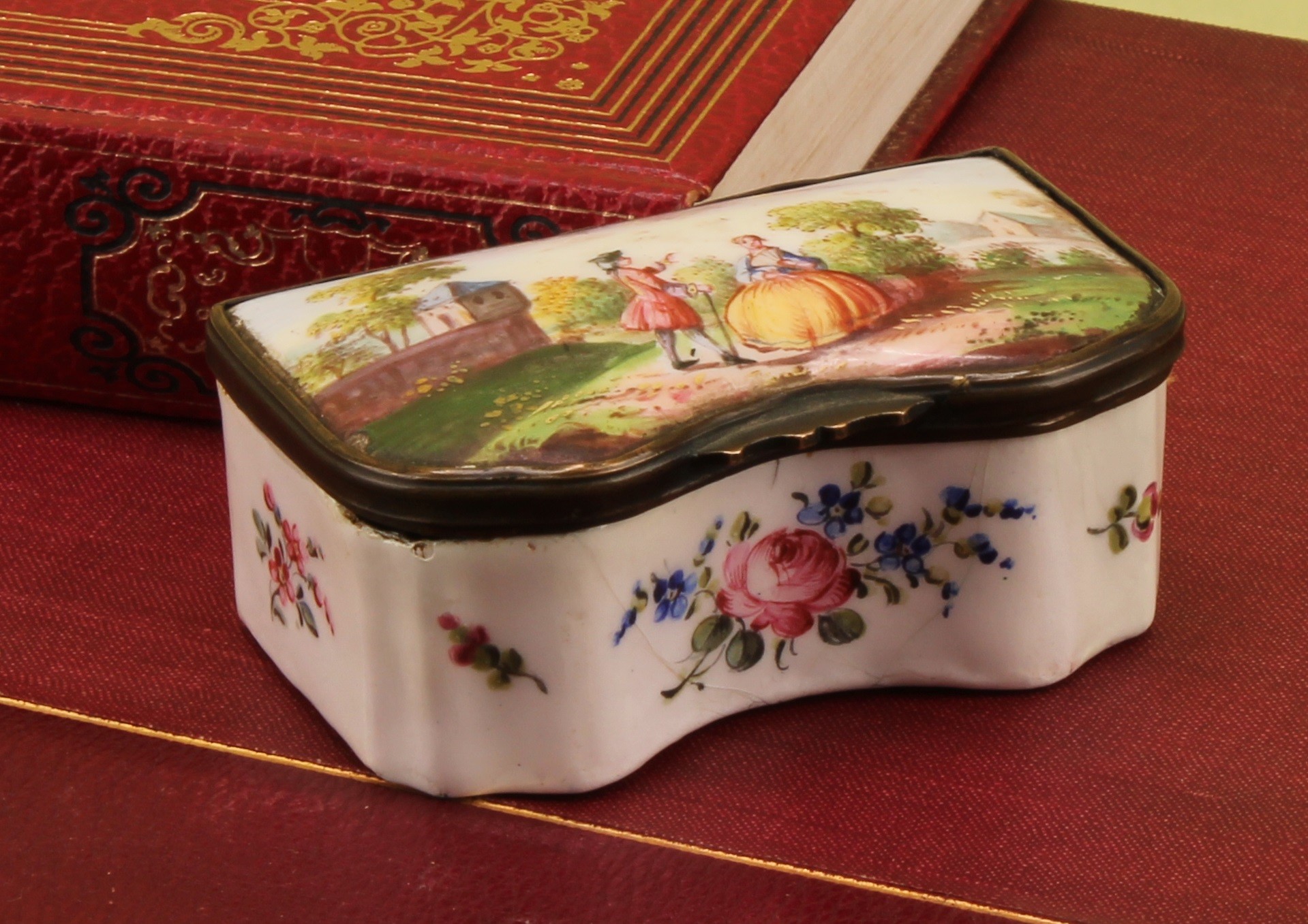 A 19th century enamel serpentine table snuff box, hinged cover painted in polychrome with a courting couple in a landscape, the base with sprigs and sprays, 7.5cm wide,