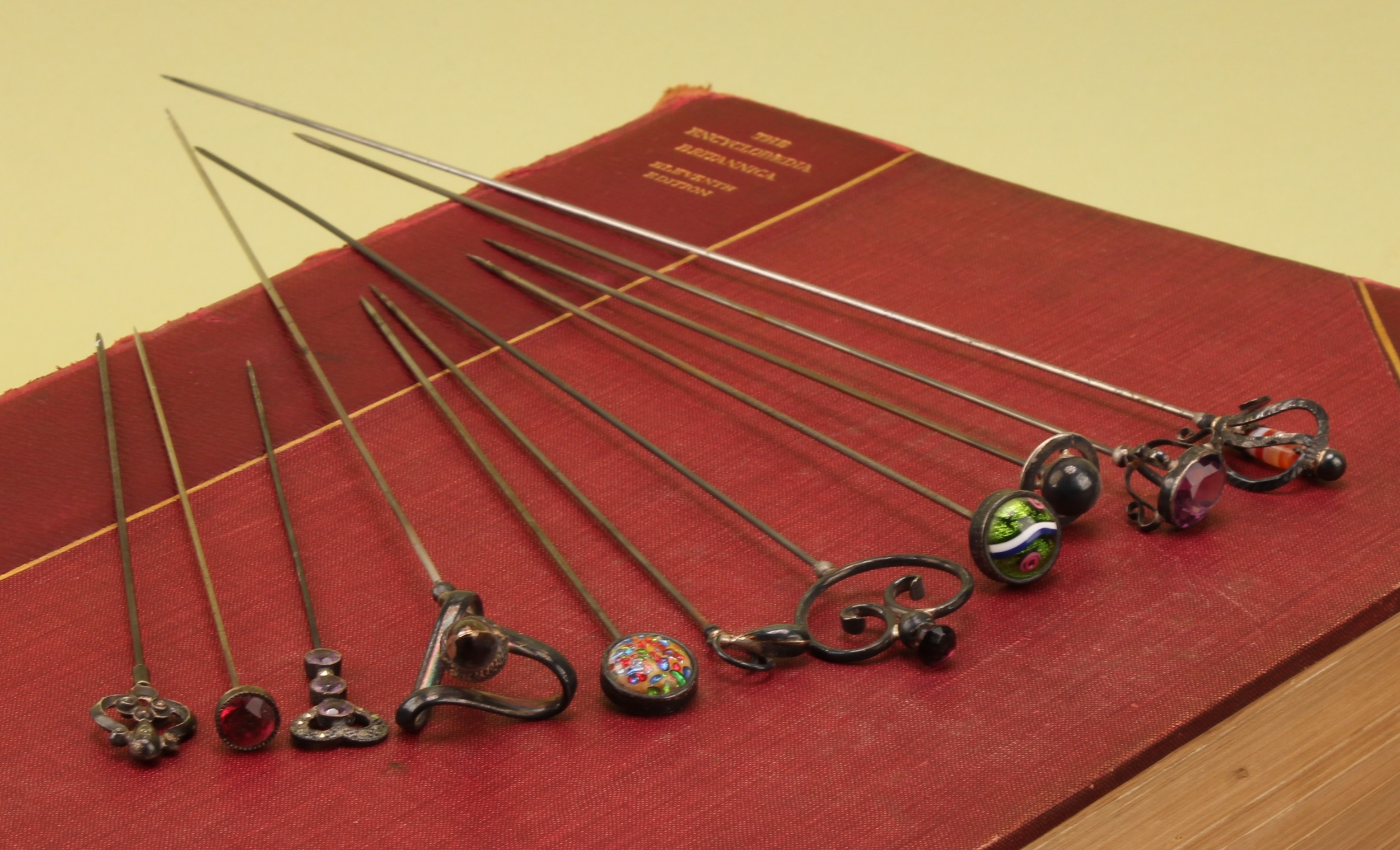 An Edwardian silver and agate hat pin, modelled as a basket hilt sword, 28.5cm long, Joseph Cook & Son, Birmingham 1908; an Art Nouveau silver hat pin, 24cm long, Frederick Banks, 1908; a Continental silver and glass swivel top hat pin; another; other silver topped hat pins (11)