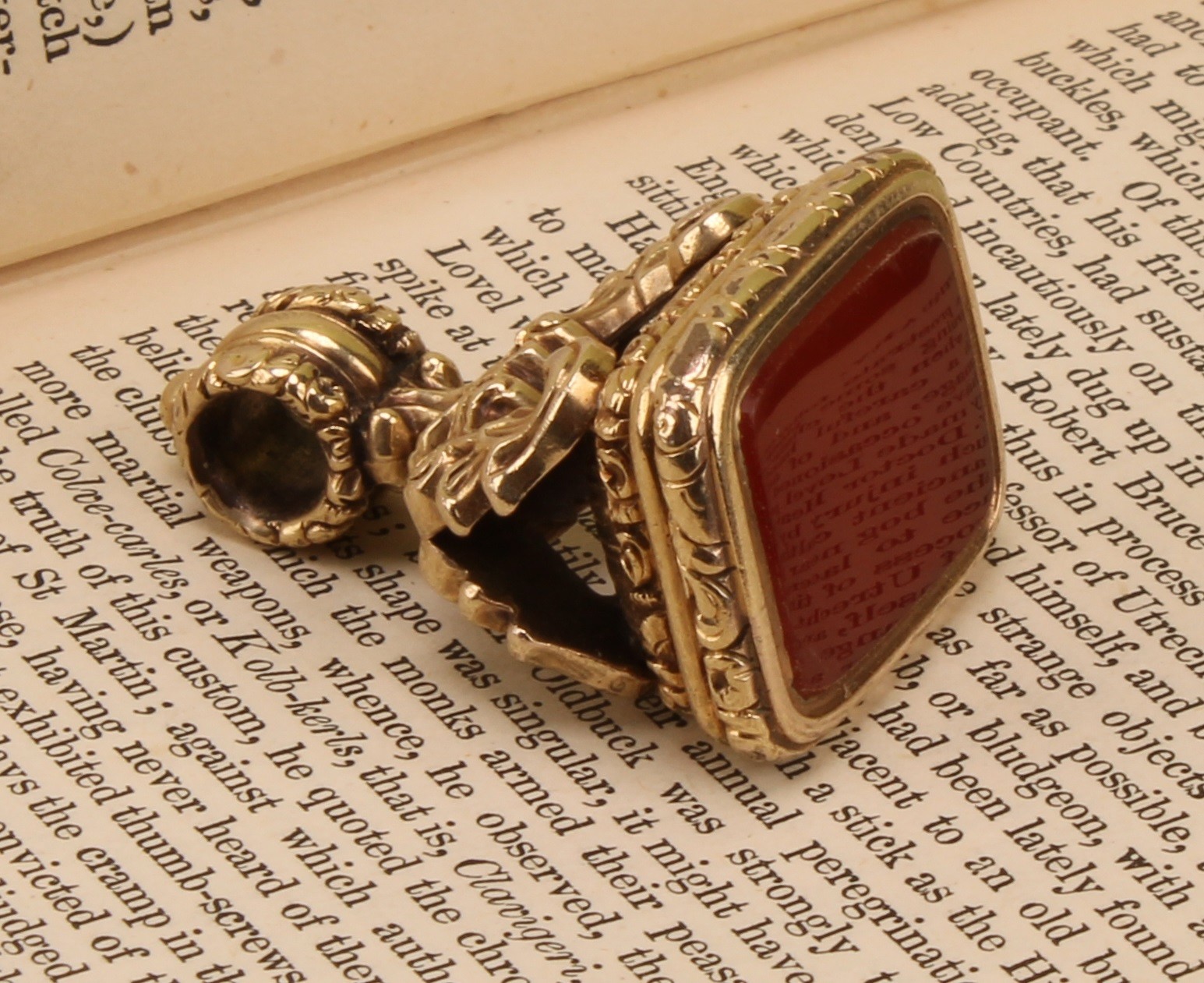An early 19th century gold coloured metal fob seal, chased with scrolling foliage, rounded rectangular carnelian matrix, 3.5cm over loop, 2.5cm wide, c.1820