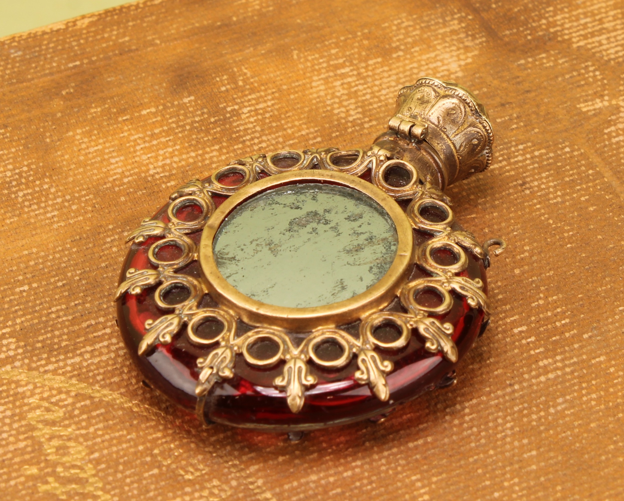 A 19th century Continental gilt metal mounted ruby glass moon shaped scent bottle, centred by a mirror, hinged cover, 6.5cm long, c.1870