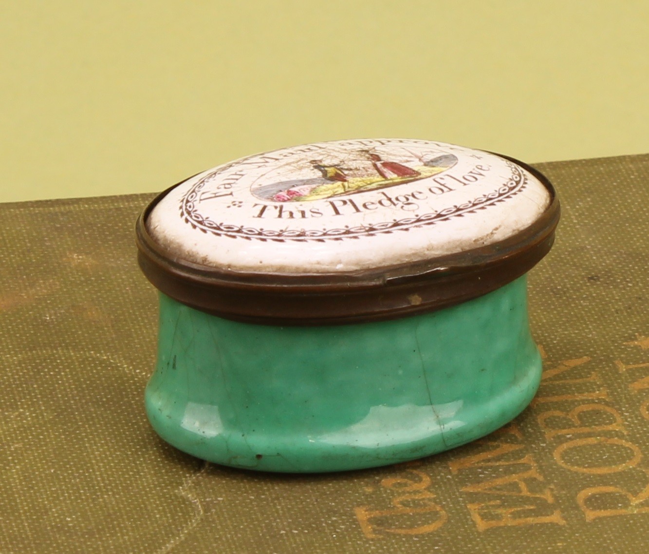 A George III South Staffordshire enamel oval patch box, hinged cover transfer printed with a courting couple, and the inscription Fair Maid approve This Pledge of love (sic), green base, 4.5cm wide, c.1800