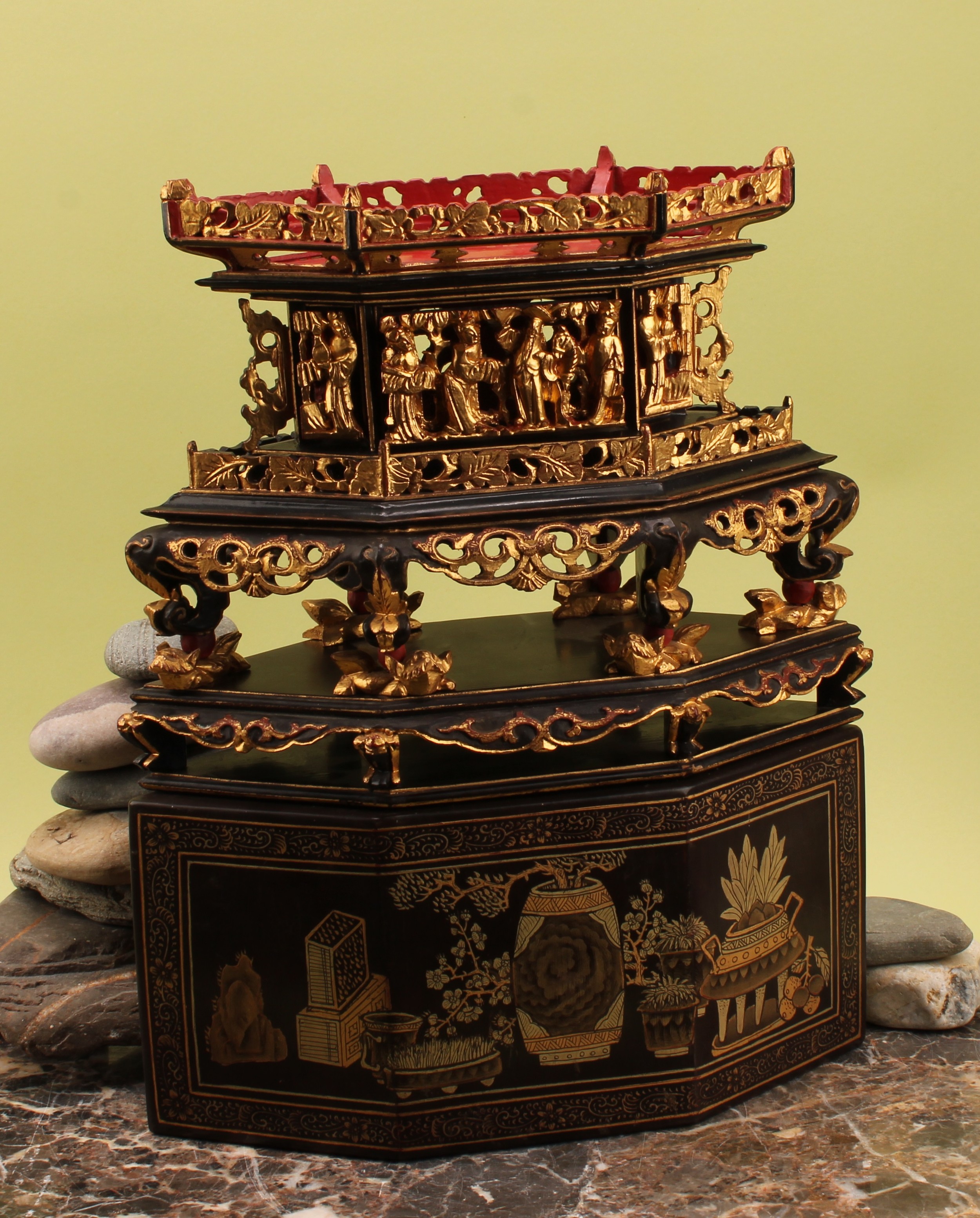 A Chinese lacquer and giltwood offering stand, galleried top pierced with leaves above a carved frieze with an altar flanked by two monks, six scrolling supports on foo dog feet, plinth base, the stand hand-painted with two panels of garden birds among leaves and ancient playthings within scrolling ruyi borders, 41.5cm high overall, 33cm wide, signed interior, c. 1900