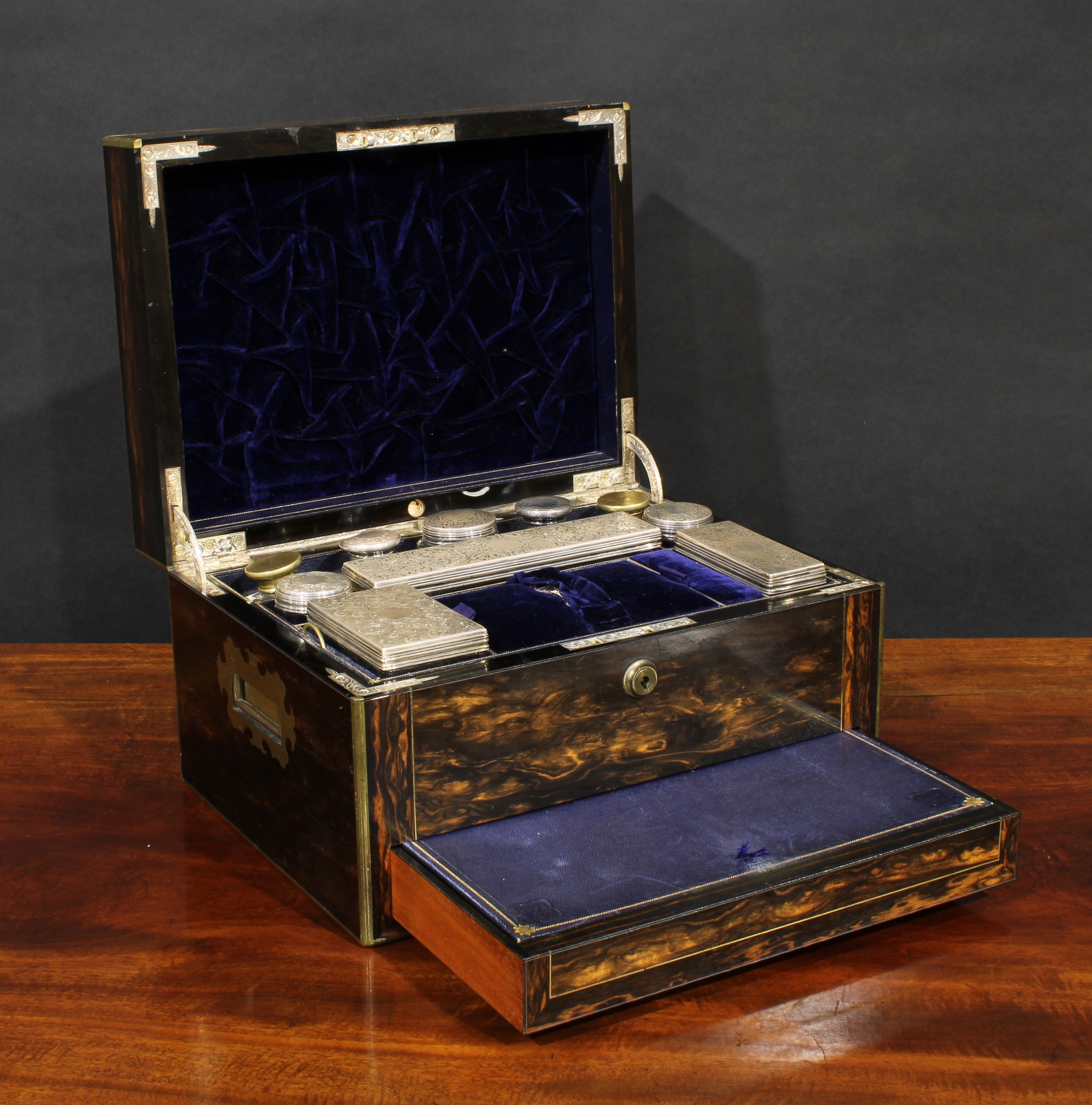 A Victorian brass mounted coromandel dressing case, hinged cover enclosing an assortment of silver and other metal mounted glass boxes and bottles, the drawer enclosing provisions for a pocket watch and jewellery, 18cm high, 31cm wide, 23.5cm deep, c.1870