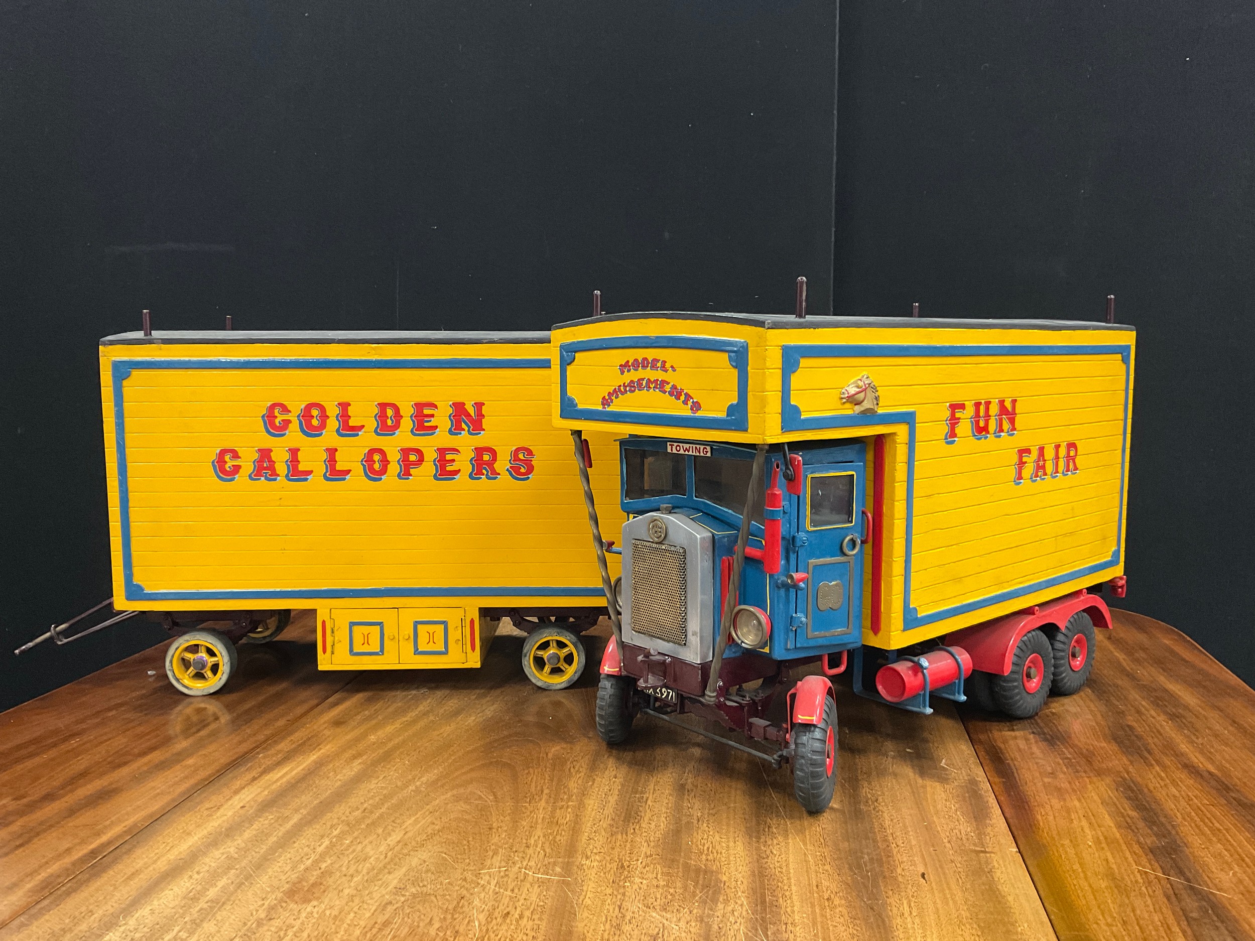 A handmade scratch built model, of a Fairground transport wagon and trailer, made by Geoff Cocker from Eyam Derbyshire, metal chasse, wooden cab and coach work, Fun Fair, Amusements on Tour, red and blue lettering, yellow ground, 34cm high, 110.5cm long, 20.5cm wide