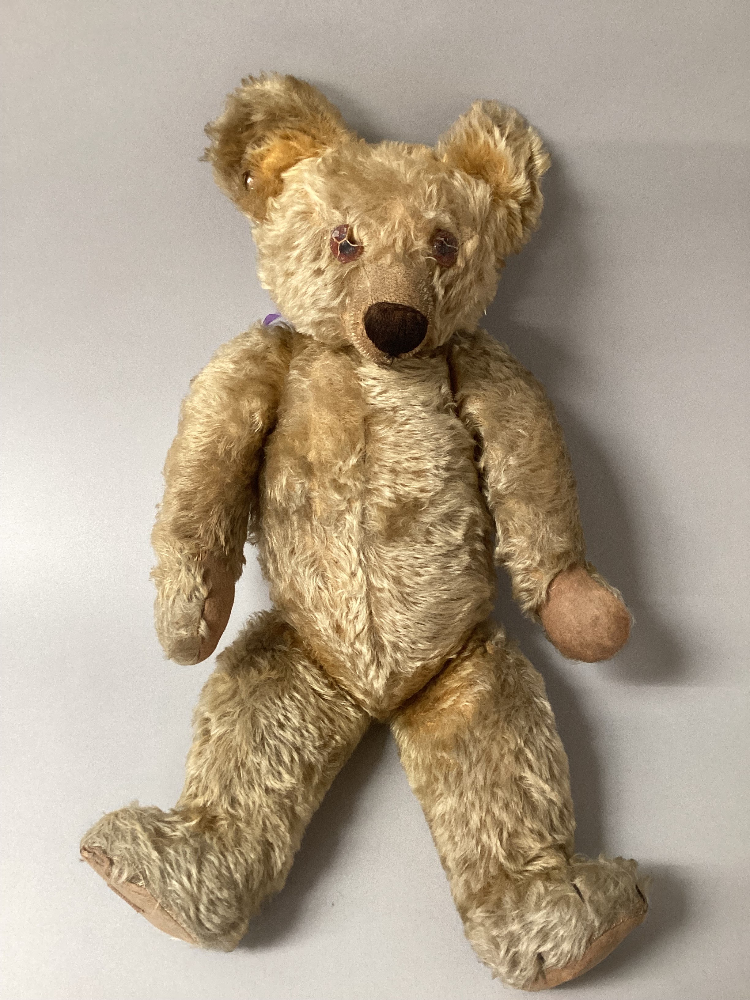 An Antique 1930 Chad Valley golden mohair jointed teddy bear,  has damaged amber glass eyes,small hump, good overall coat with some black claws remaining , good cup ears with celluloid 1930 button in right ear-see photograph , all original felt pads and cropped shaved muzzle with good snout stitching, flat footed with red Chad valley 1930 foot label and from The wonderful Birmingham company started by Anthony Bunn in the 19thC, 62cm high overall, label to foot. (1)